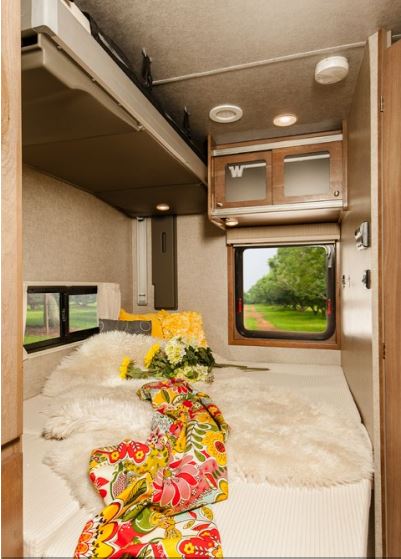 Cozy RV bedroom with plush bed, floral throw, and scenic windows. Ideal for an RV rental adventure.. Winnebago Brave 2015