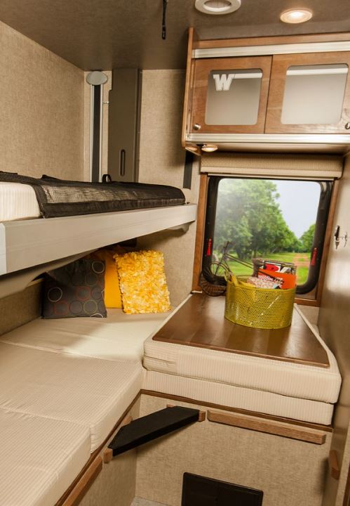 Explore this rv rental's compact interior: bunk beds, cozy L-shaped seating, and a table with a scenic window view.. Winnebago Brave 2015