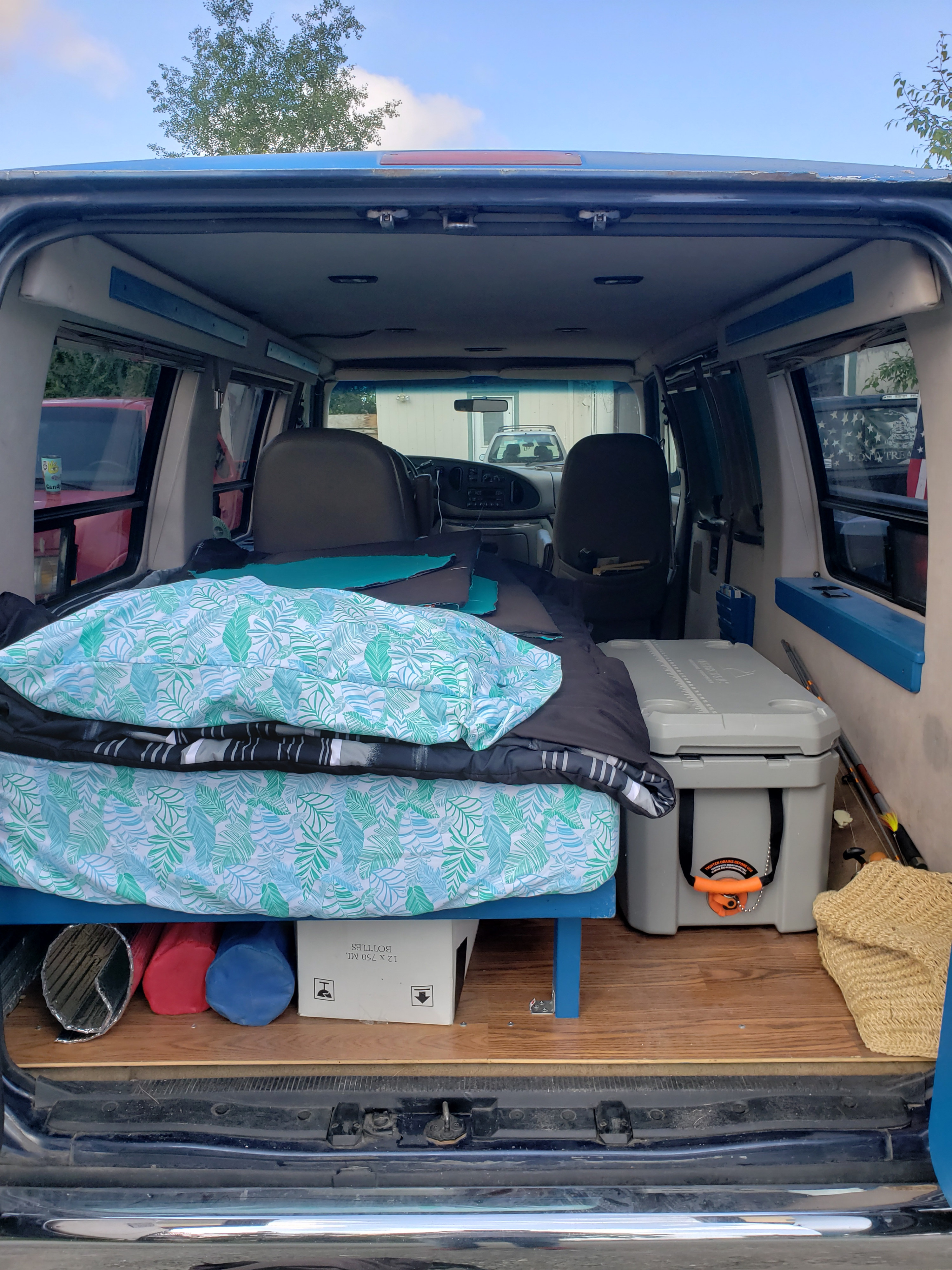 Cozy van interior, ideal for rv rental, featuring a comfortable bed, large cooler, and under-bed storage.. Ford Econoline Club Wagon 1998