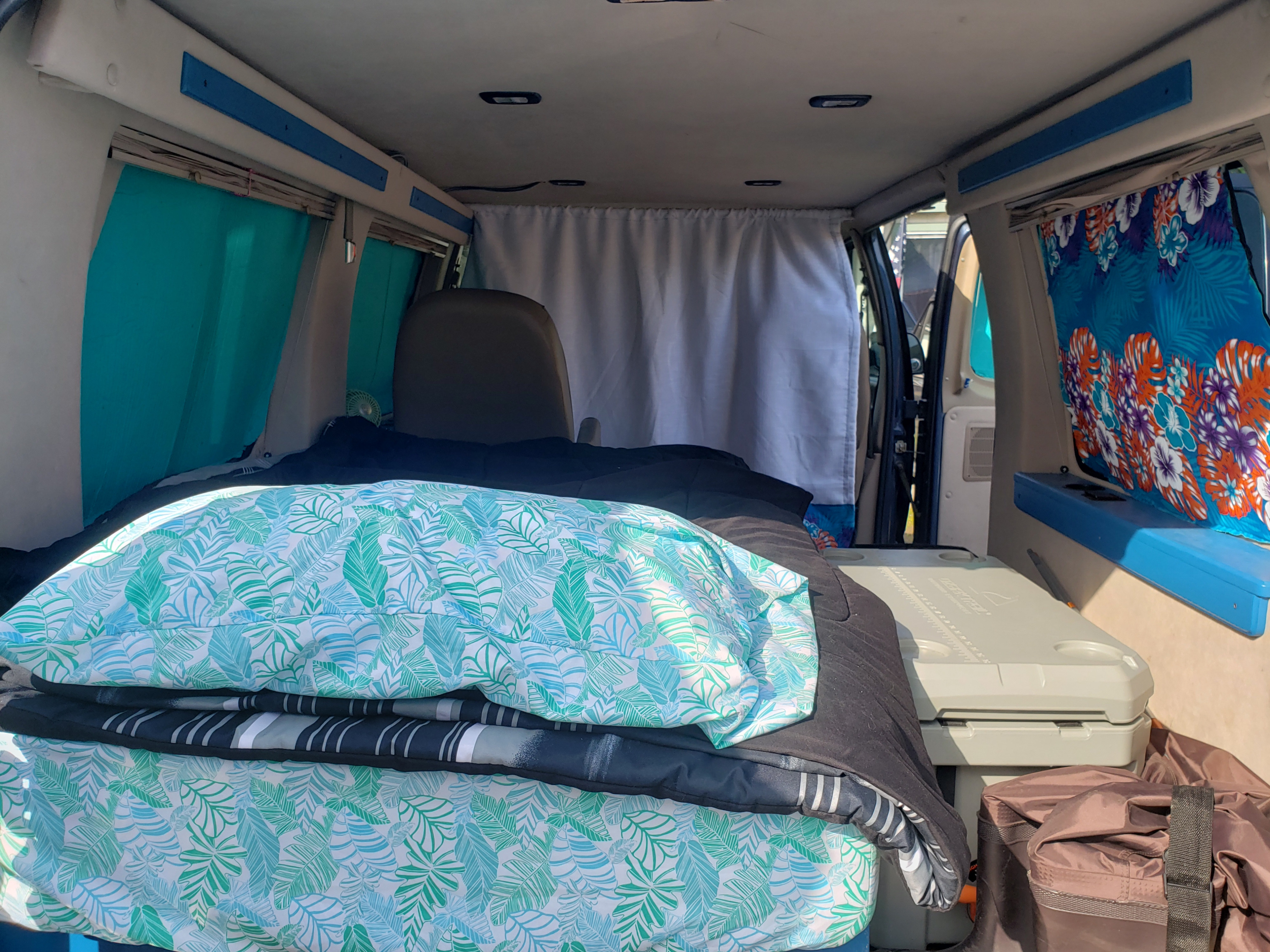 RV rental van interior: tropical bed, privacy curtain, and cooler for a comfortable mobile living.. Ford Econoline Club Wagon 1998
