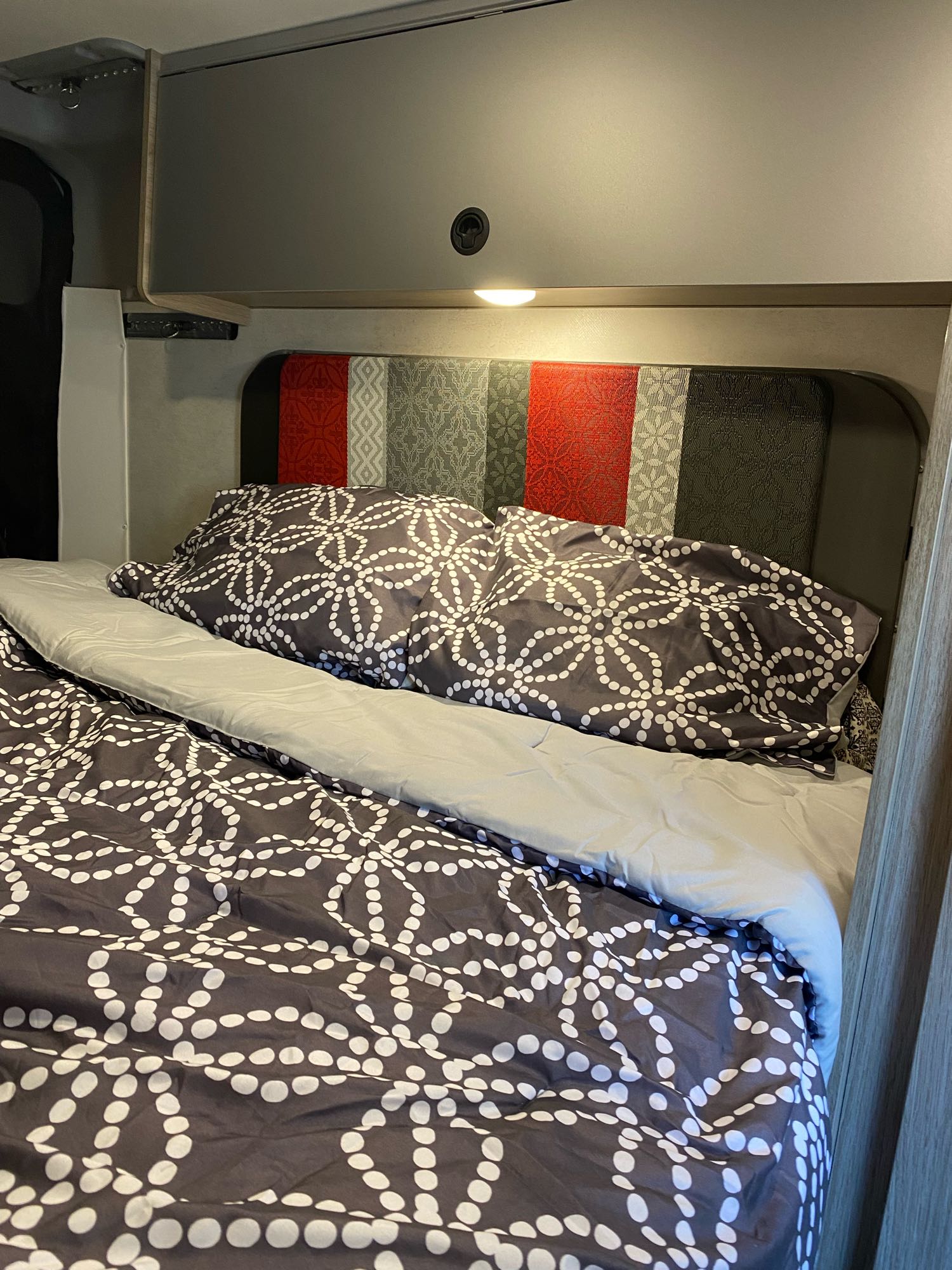 Cozy RV rental bedroom with patterned bedding, colorful headboard, and overhead storage. Ideal for a compact, comfortable stay.. Winnebago Other 2022