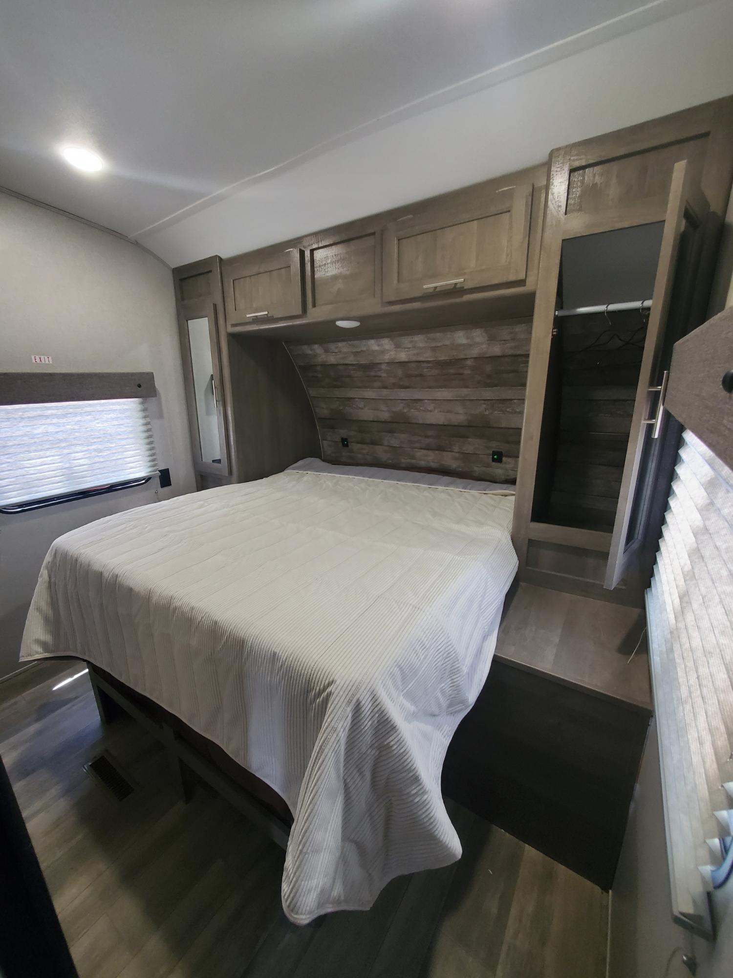 Comfortable RV rental bedroom featuring a large bed, overhead cabinets, and a compact wardrobe with a mirror.. Forest River Other 2021