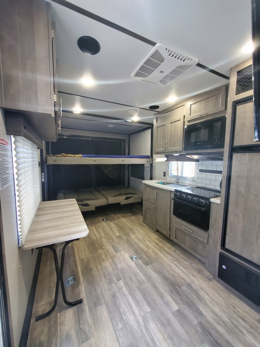 Modern RV rental interior featuring a full kitchen, convertible bunk beds, and dining area on wood-look flooring.. Forest River Other 2021