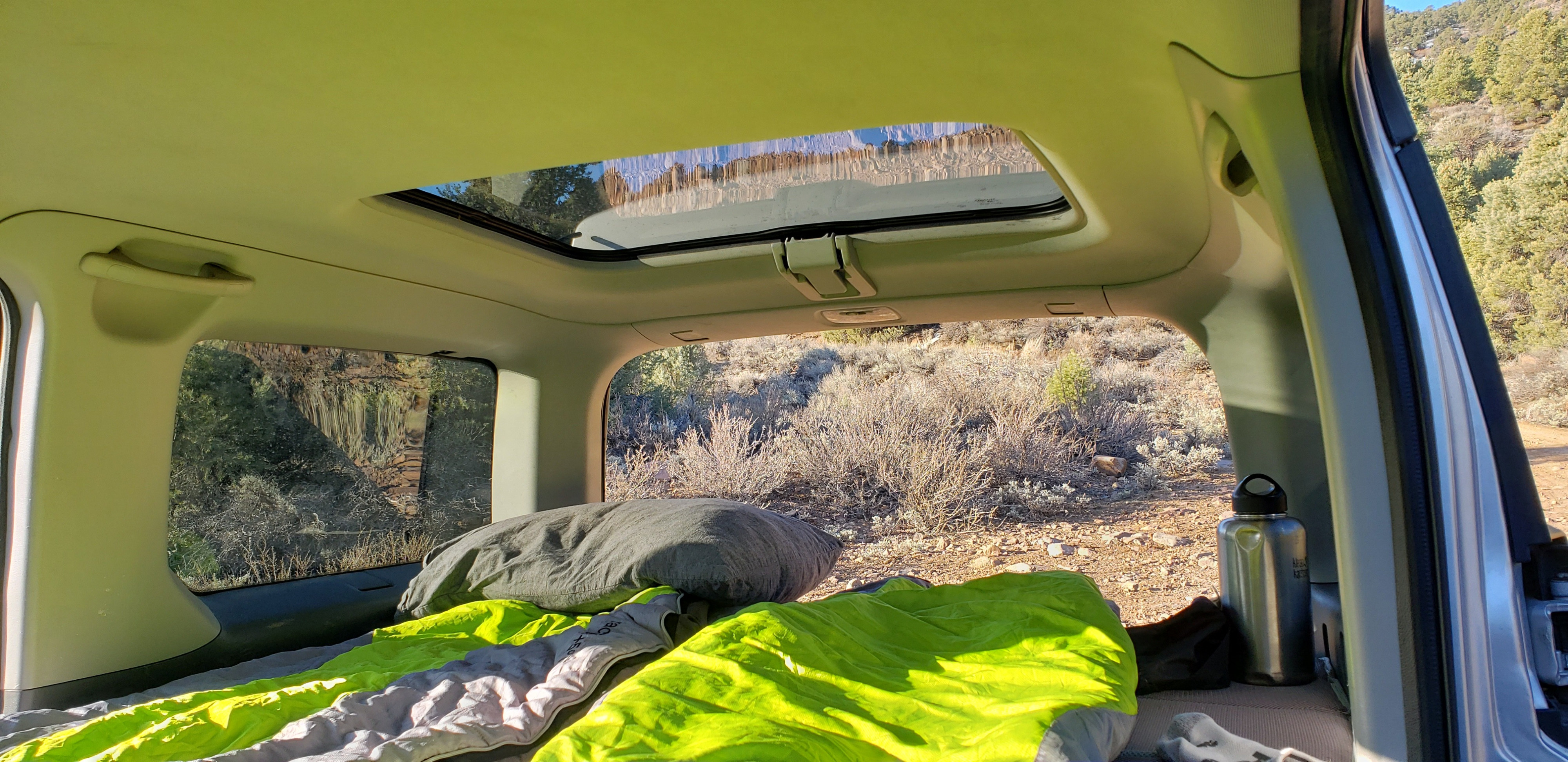 Cozy rv rental interior setup for car camping with a sleeping pad, pillow & bottle. Views of arid outdoor landscape.. Honda Element 2003