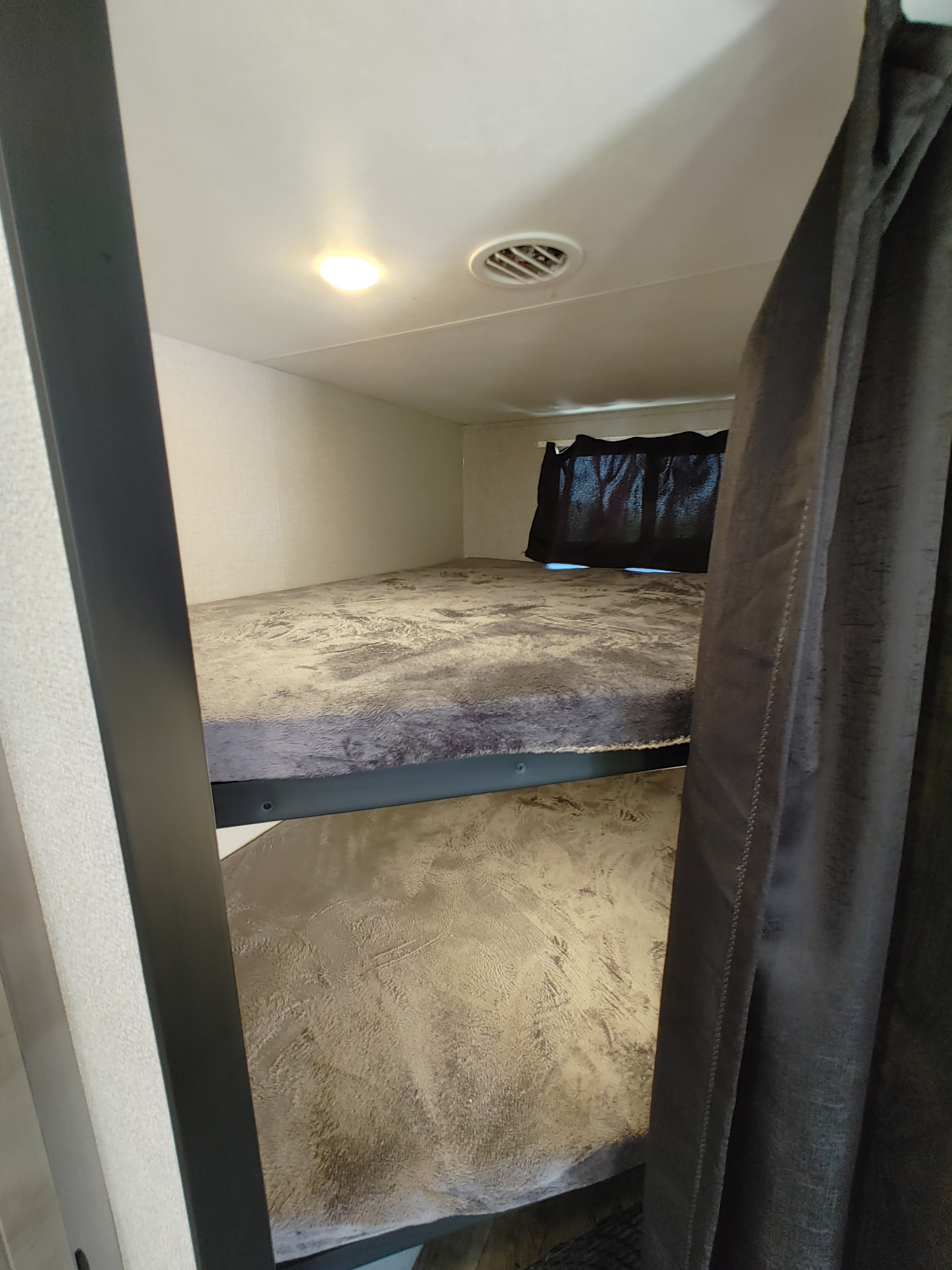 RV rental bunk beds feature patterned bedding, a window curtain, ceiling light, and vent, offering cozy sleeping space.. Starcraft Travel Trailer 2021