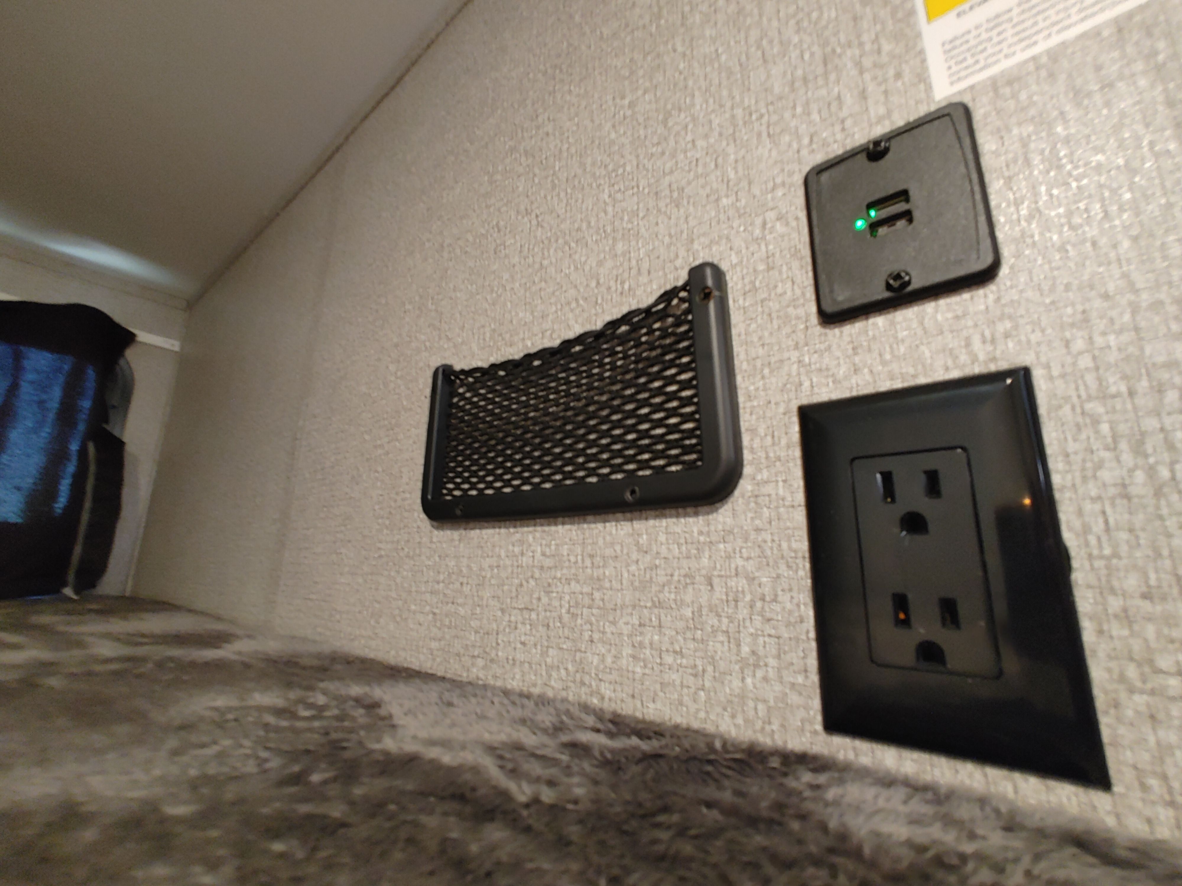 RV rental bunk area: Charging station with USB ports (green lights visible), an electrical outlet, and a mesh storage net for convenience.. Starcraft Travel Trailer 2021