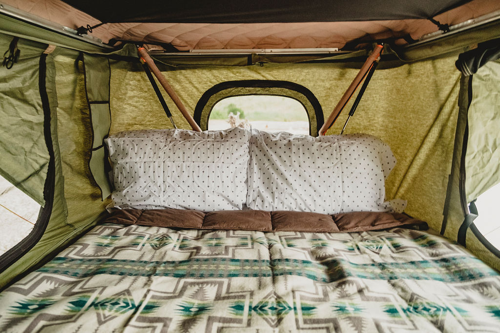 Inside this cozy rv rental roof-top tent: patterned pillows, a geometric blanket, and a window view, ready for travel.. Toyota 4 Runner 2003