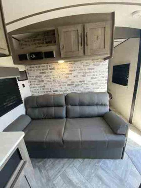 Comfortable RV rental interior with a grey sofa, overhead cabinets, and brick accent wall, perfect for your next adventure.. Keystone Springdale 2021