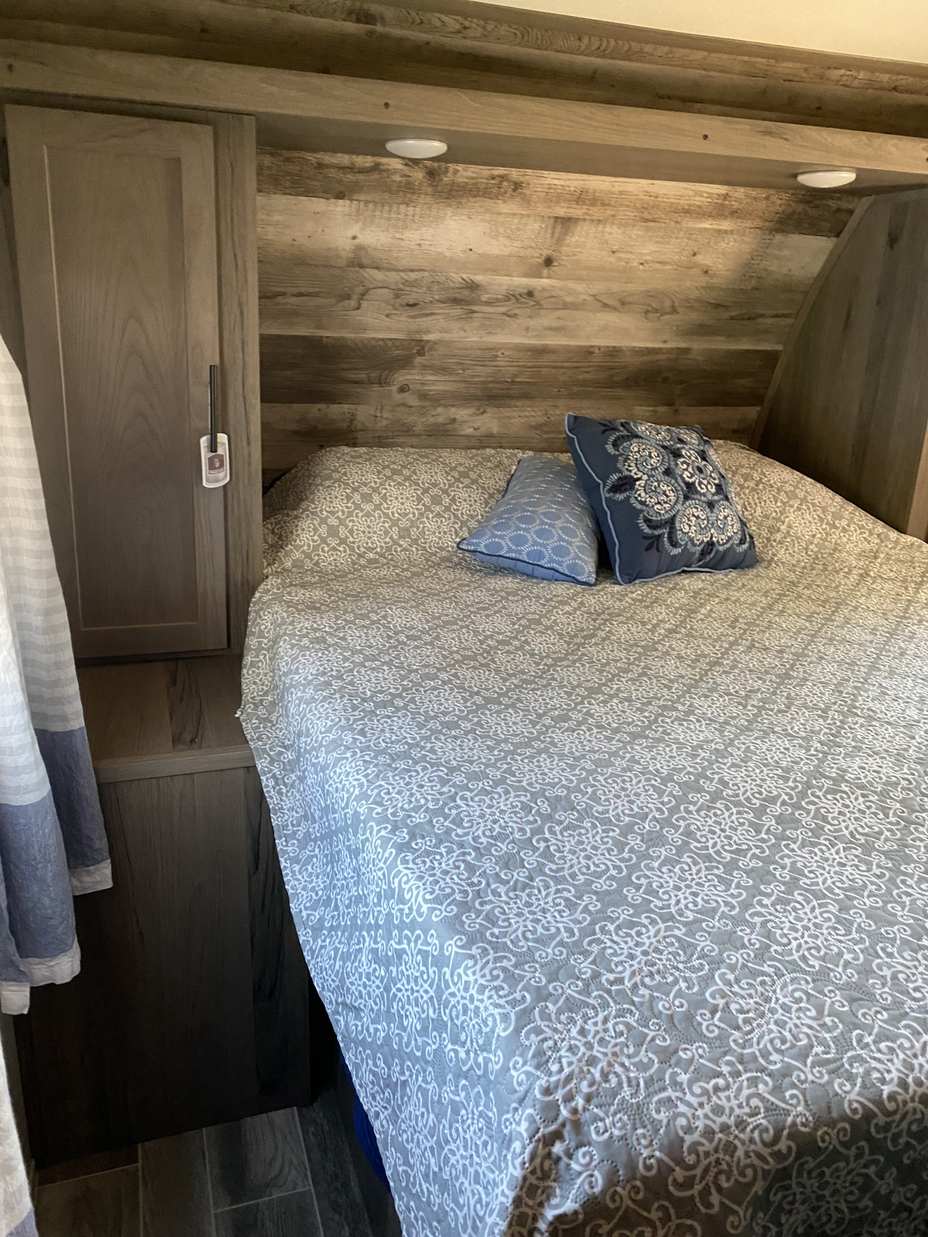 Cozy RV rental bedroom features a bed with patterned comforter, blue pillows, wood accent walls, and integrated storage.. Gulf Stream Other 2021