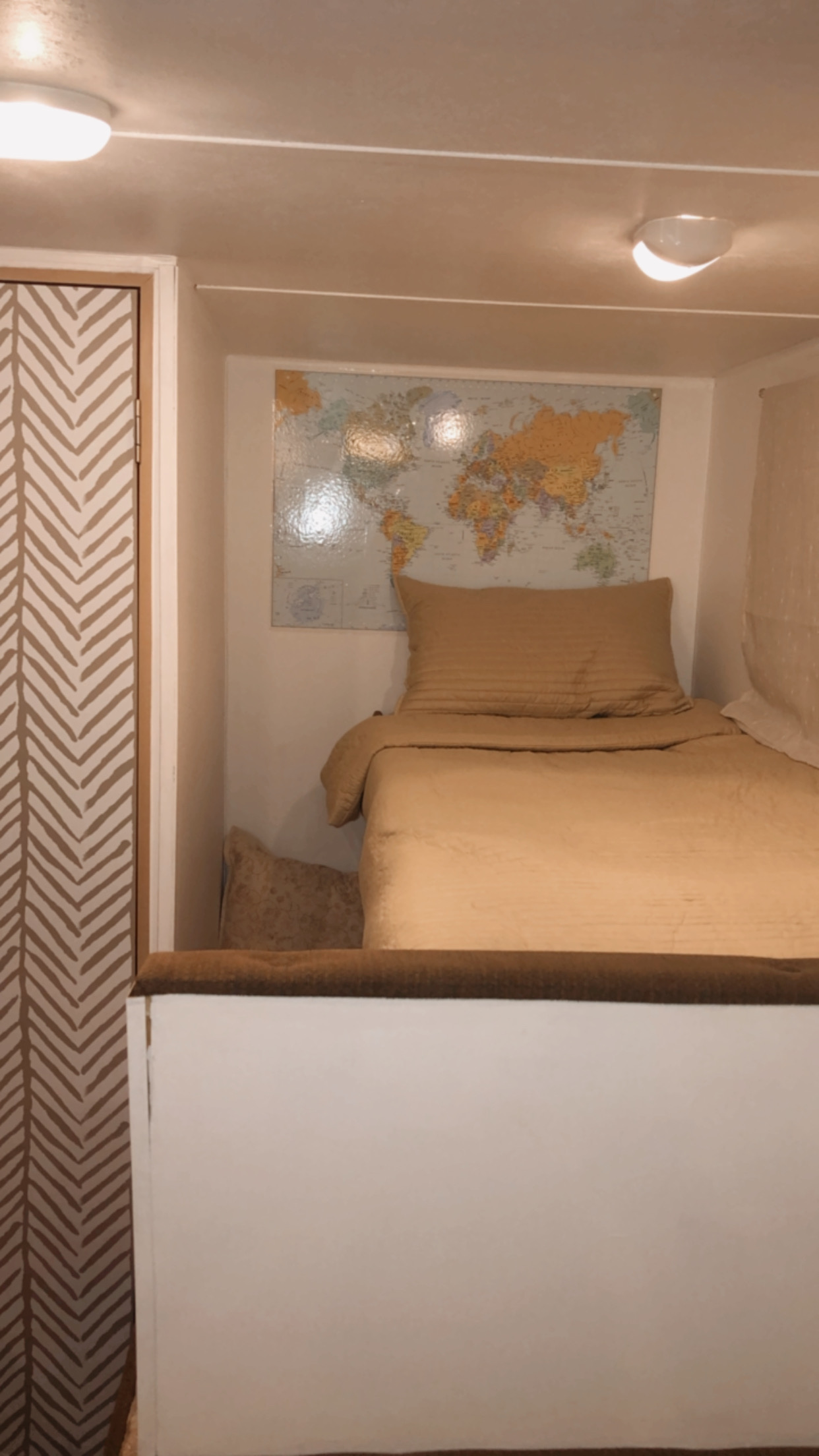 Inside a cozy **rv rental**: tan bed, world map, and chevron door. Two lights illuminate this compact sleeping area.. Wildwood 32qbss Wildwood Xlite 2014