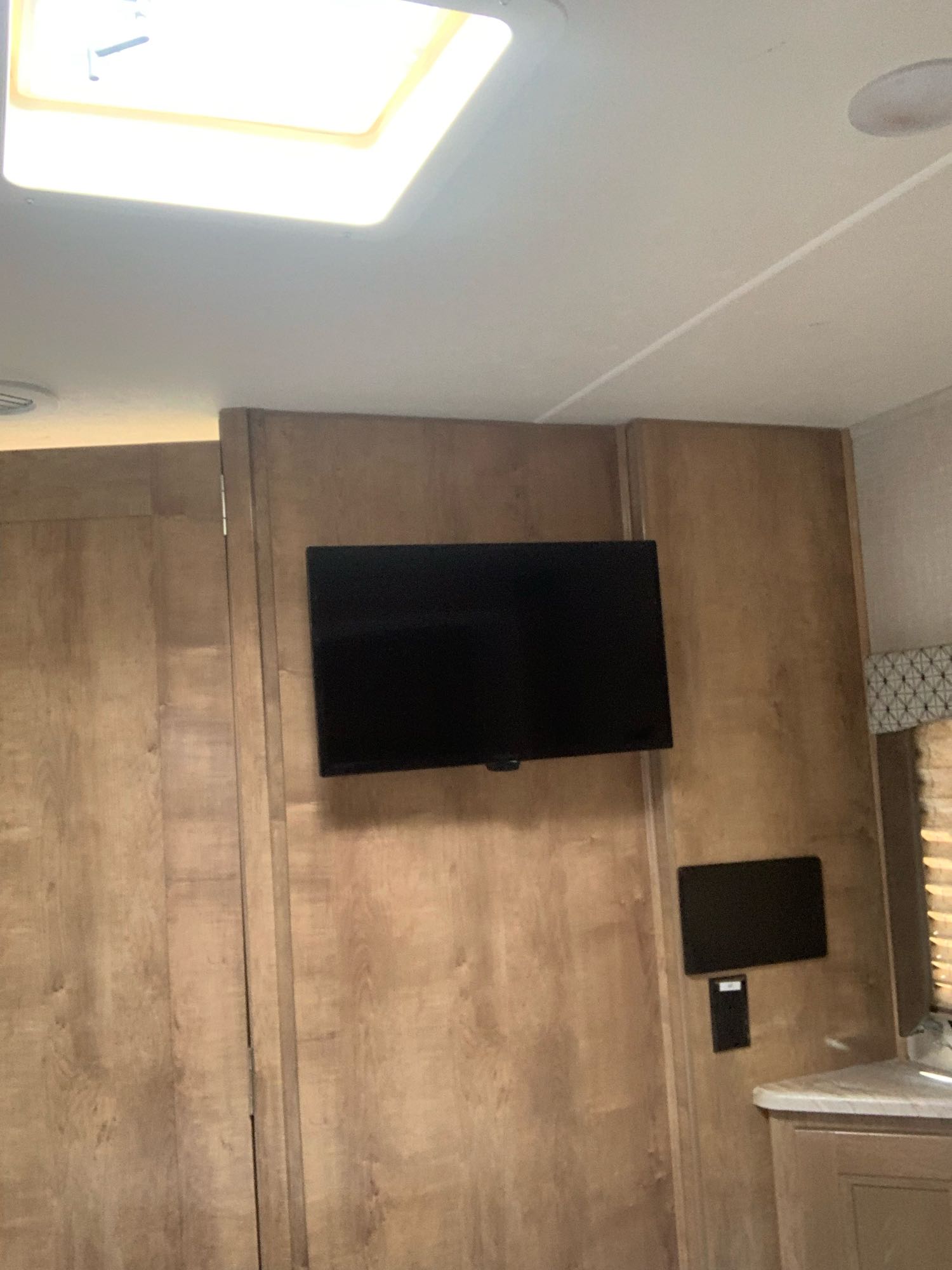RV rental interior showing a wall-mounted TV, wood paneling, ceiling vent, and window with blinds.. Forest River Coachmen Leprechaun 2020
