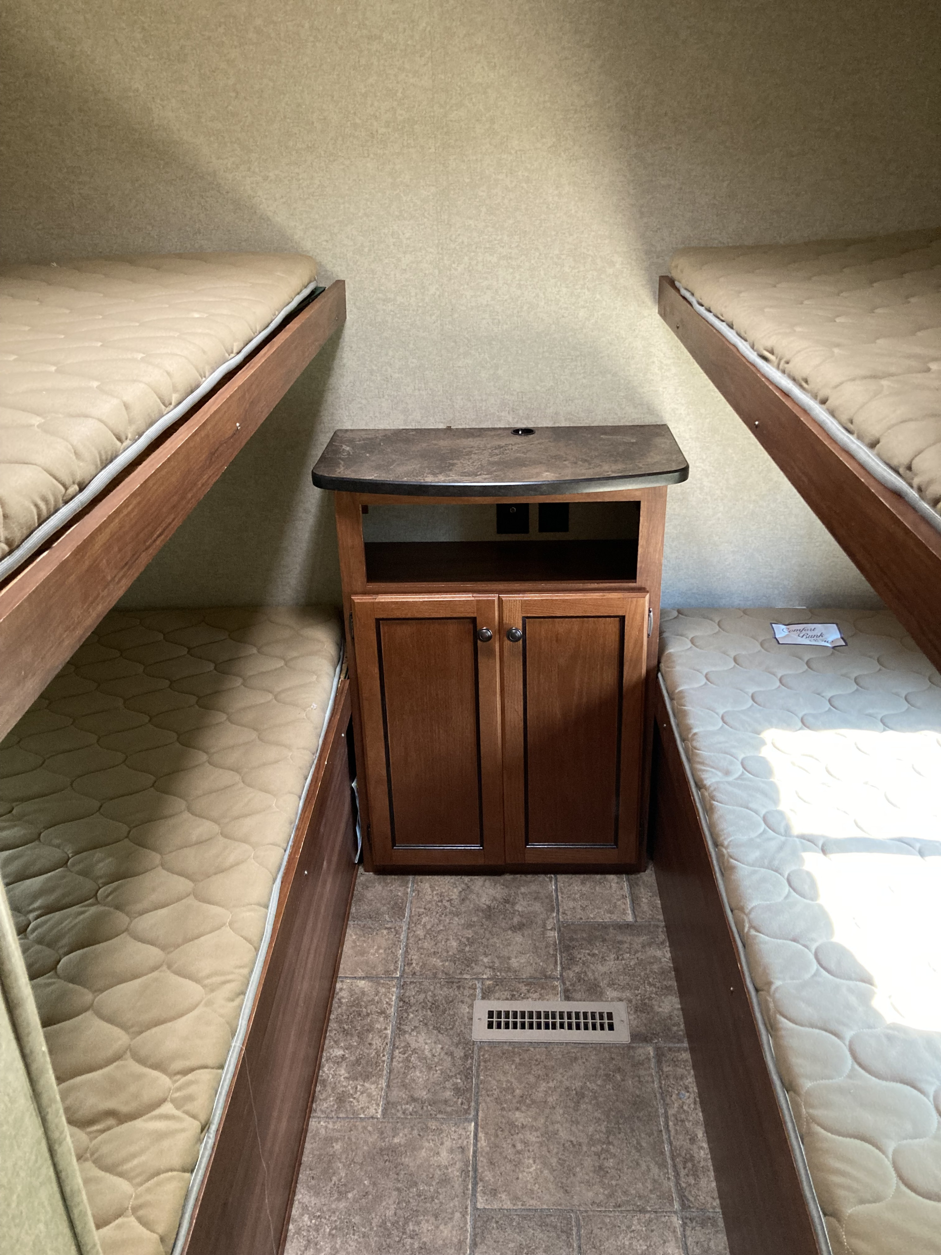 Compact RV rental bunk beds with central storage cabinet, optimizing space in a camper interior.. Heartland Trail Runner 2015