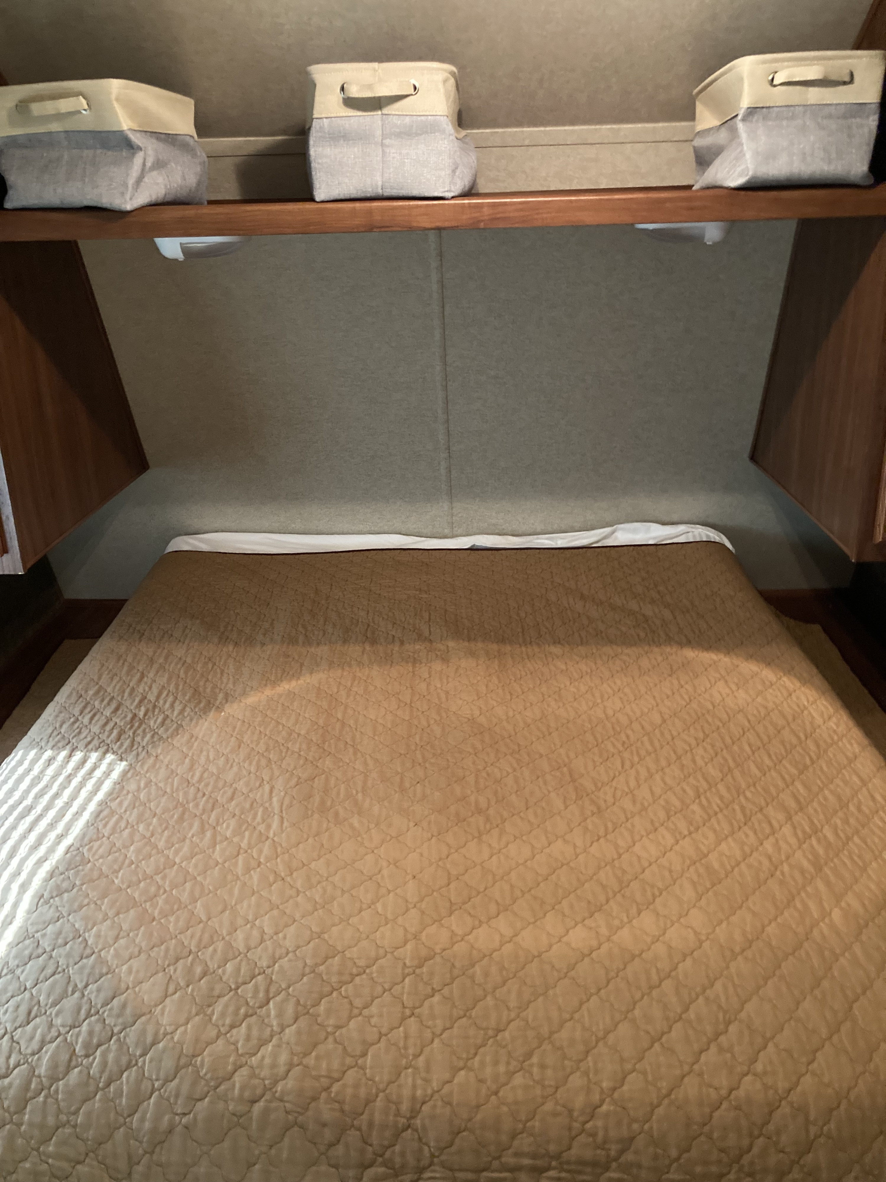 This RV rental bedroom features a cozy bed, overhead wooden shelf, and three light-colored storage bins, maximizing compact space.. Heartland Trail Runner 2015