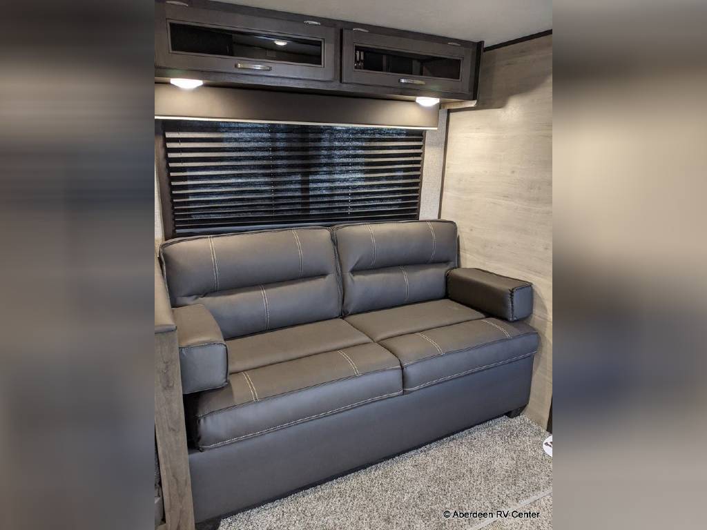 This RV rental offers a comfortable living area with a dark sofa, window blinds, and overhead storage cabinets.. Jayco Jay Flight 2021