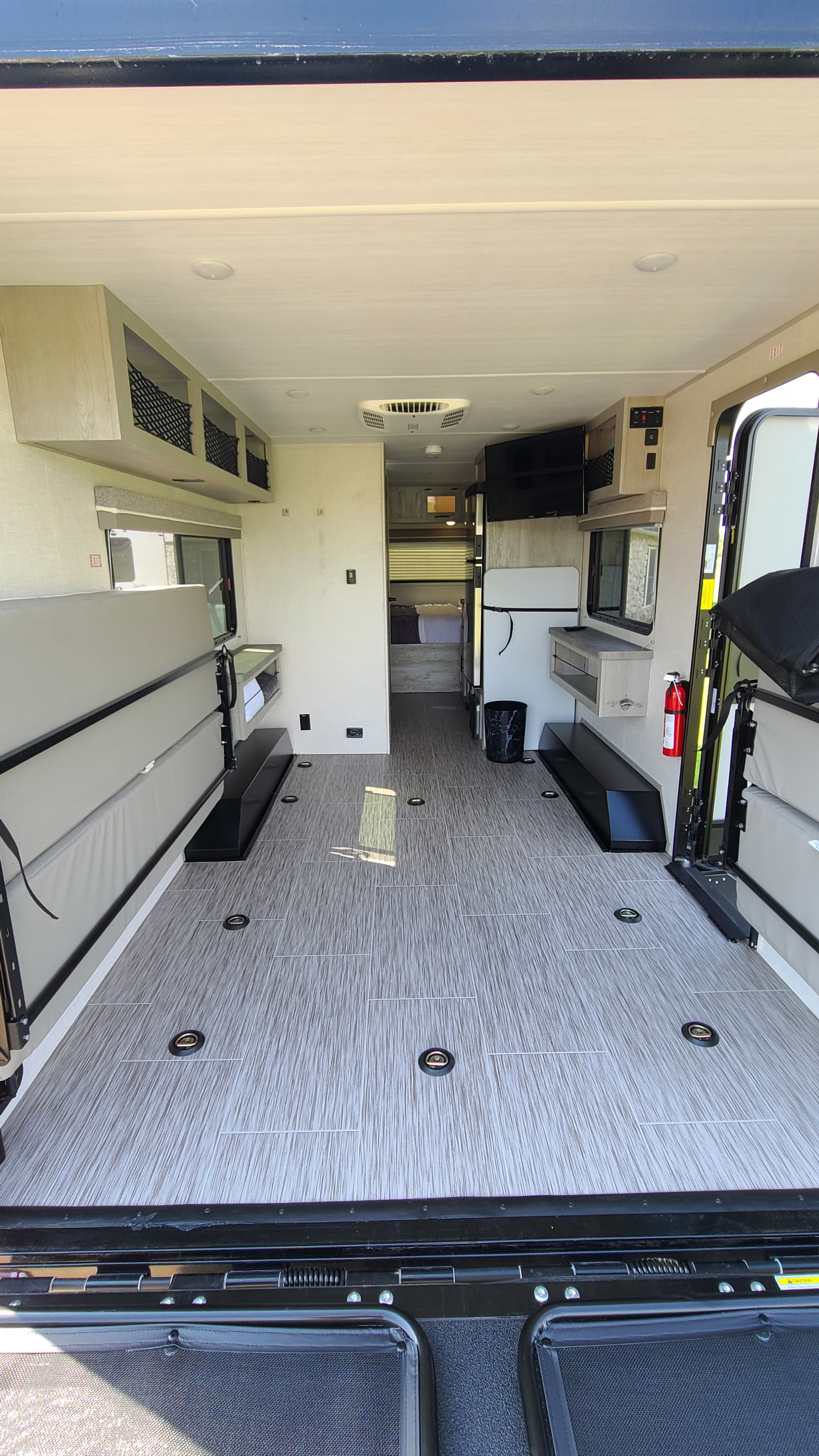 Spacious RV rental interior: a toy hauler with open cargo space, tie-downs, convertible bed, kitchen, and rear view.. Forest River Ibex 2021