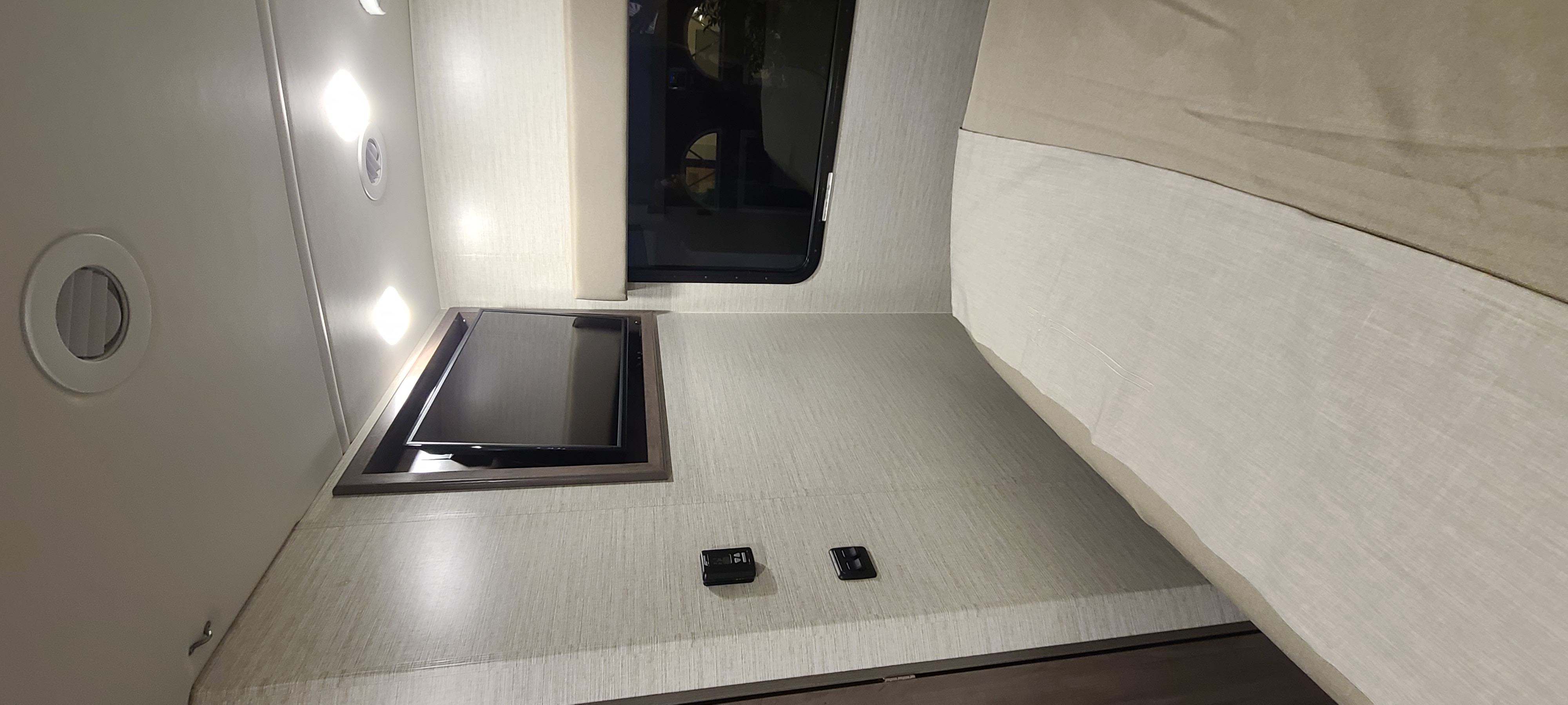 This RV rental bedroom features a mounted TV, window, bed, and lighting, perfect for travel.. Winnebago Vista 2022