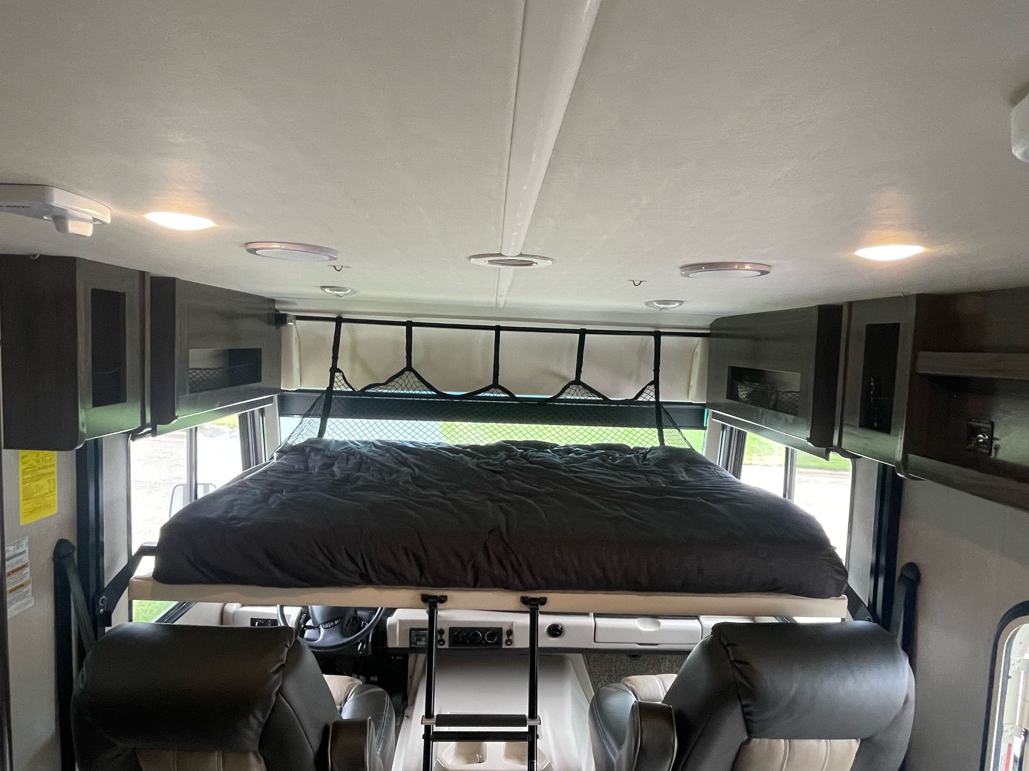 RV rental's overhead bed setup: dark bedding, safety net, and access ladder above the front seats for extra sleeping.. Holiday Rambler Admiral 2020