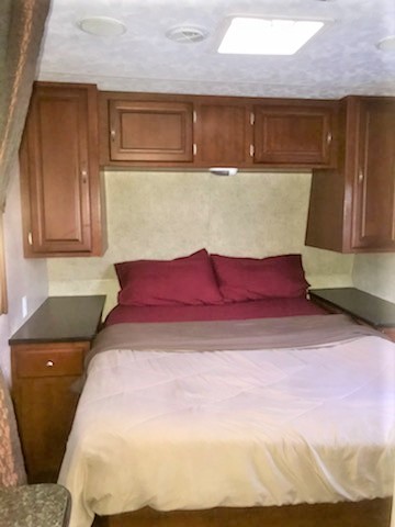Compact RV rental bedroom featuring a full bed with red pillows, built-in overhead cabinets, and side tables.. Forest River Wildwood 2010