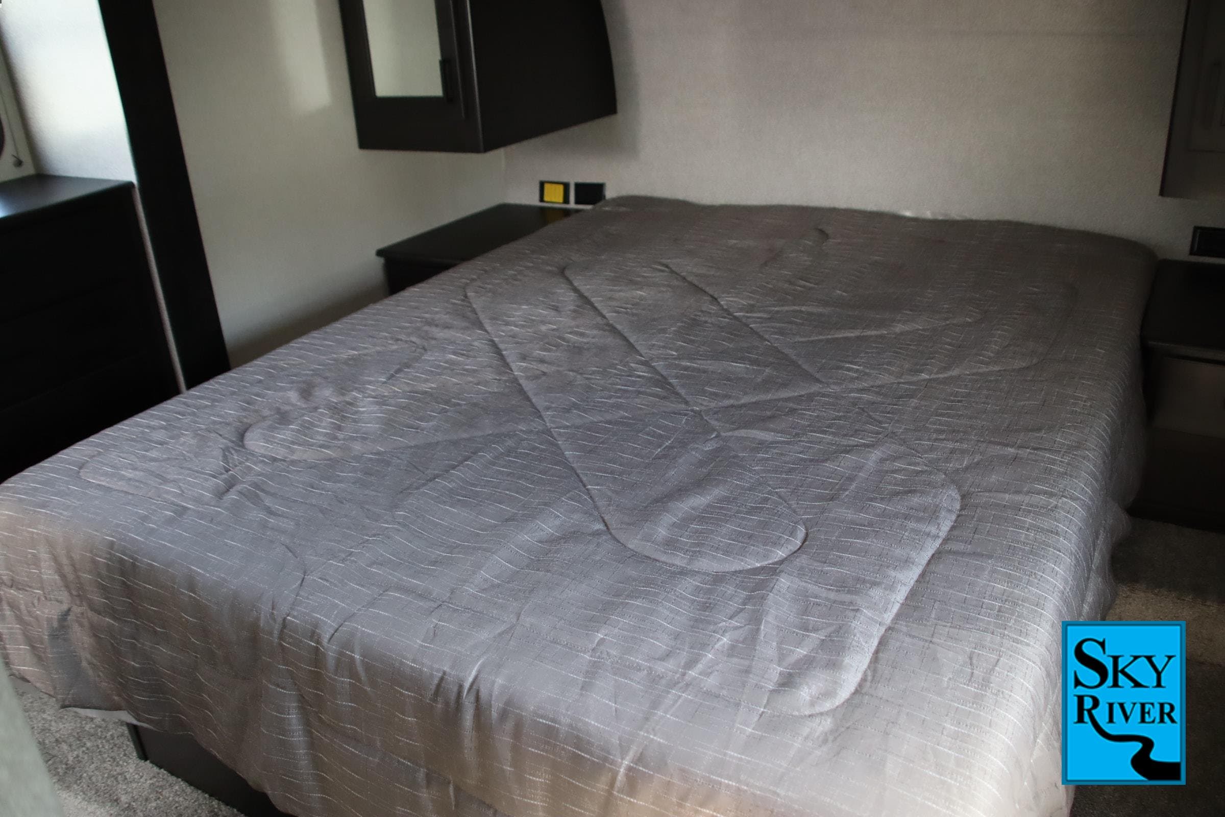 Cozy RV rental bedroom featuring a neatly made bed with a grey textured comforter and dark built-in cabinetry.. Starcraft Telluride 2021