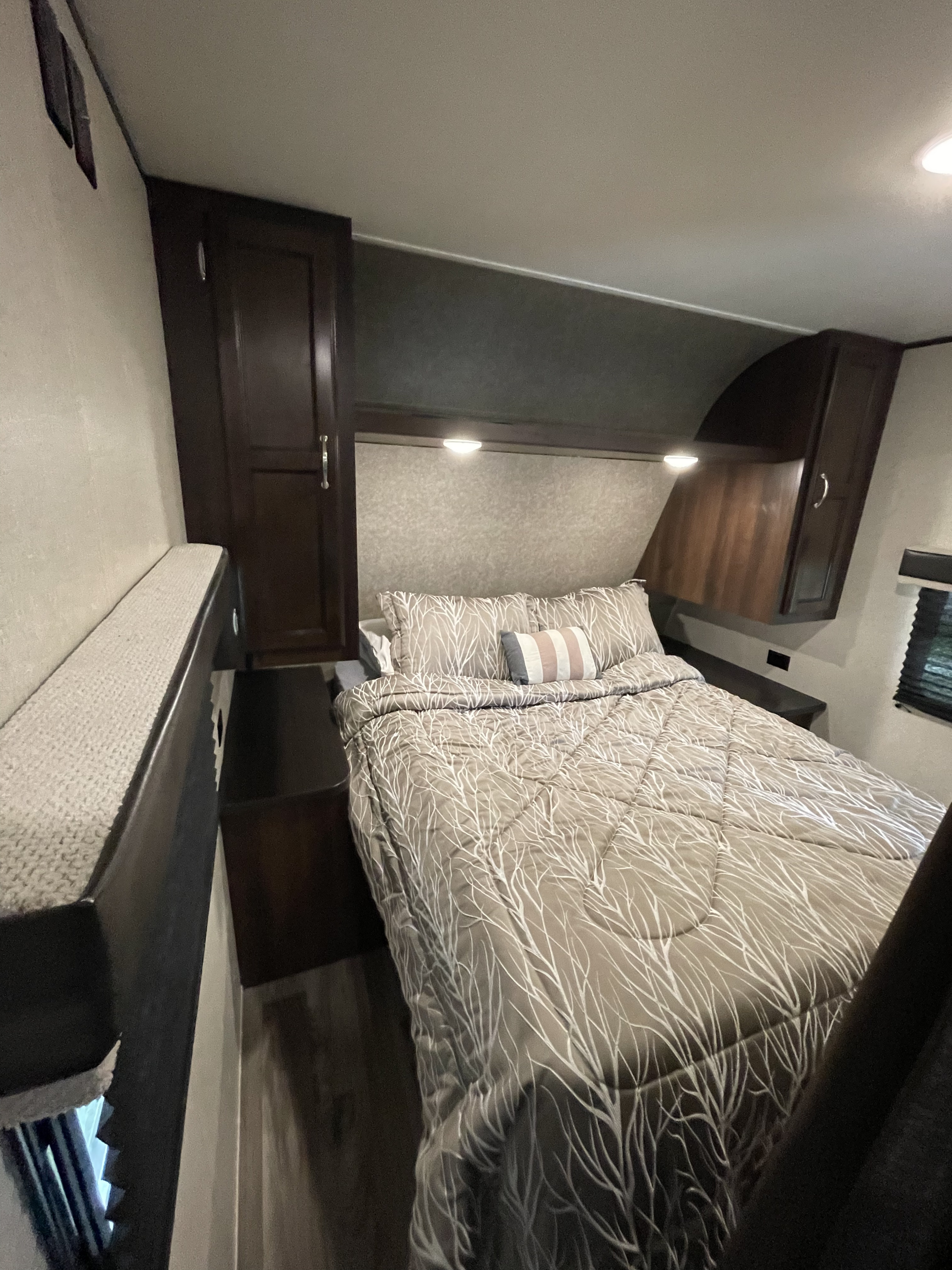 This RV rental bedroom features a comfy bed with patterned bedding, built-in cabinets, and warm lighting.. Jayco Flight SLX 2018