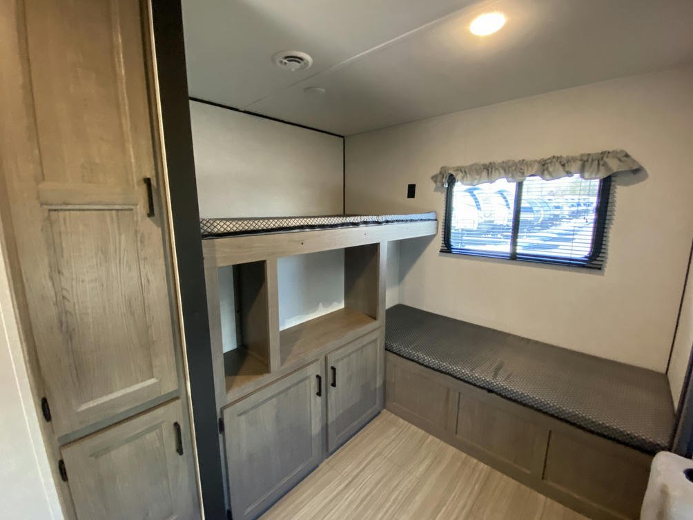 Spacious RV rental bedroom featuring bunk beds, a window, bench seating, and ample storage for comfortable travel.. Keystone Hideout 2021