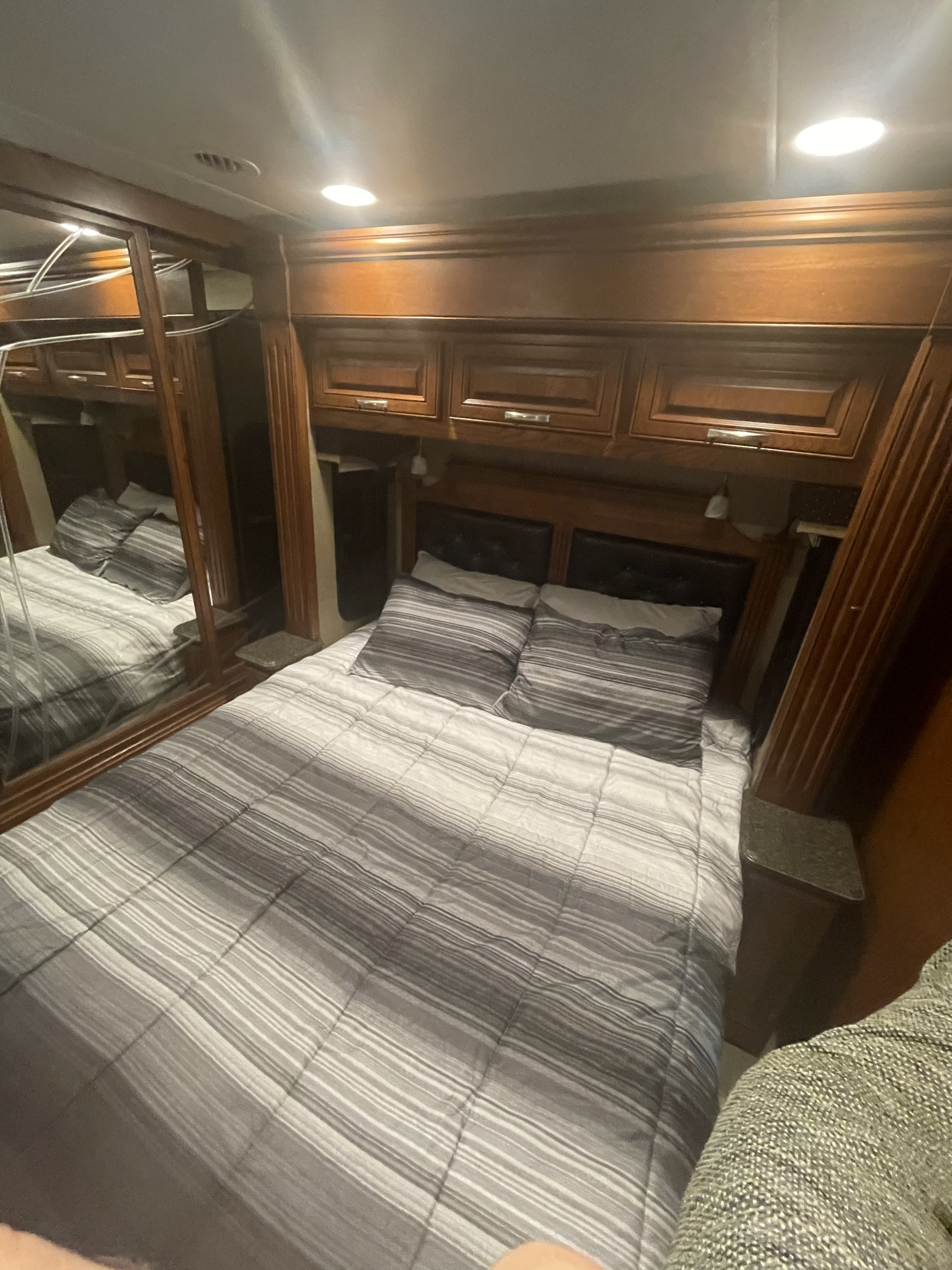 Comfortable RV rental bedroom featuring striped bedding, wooden cabinets, and bright ceiling lights, perfect for travel.. Forest River Berkshire 2016