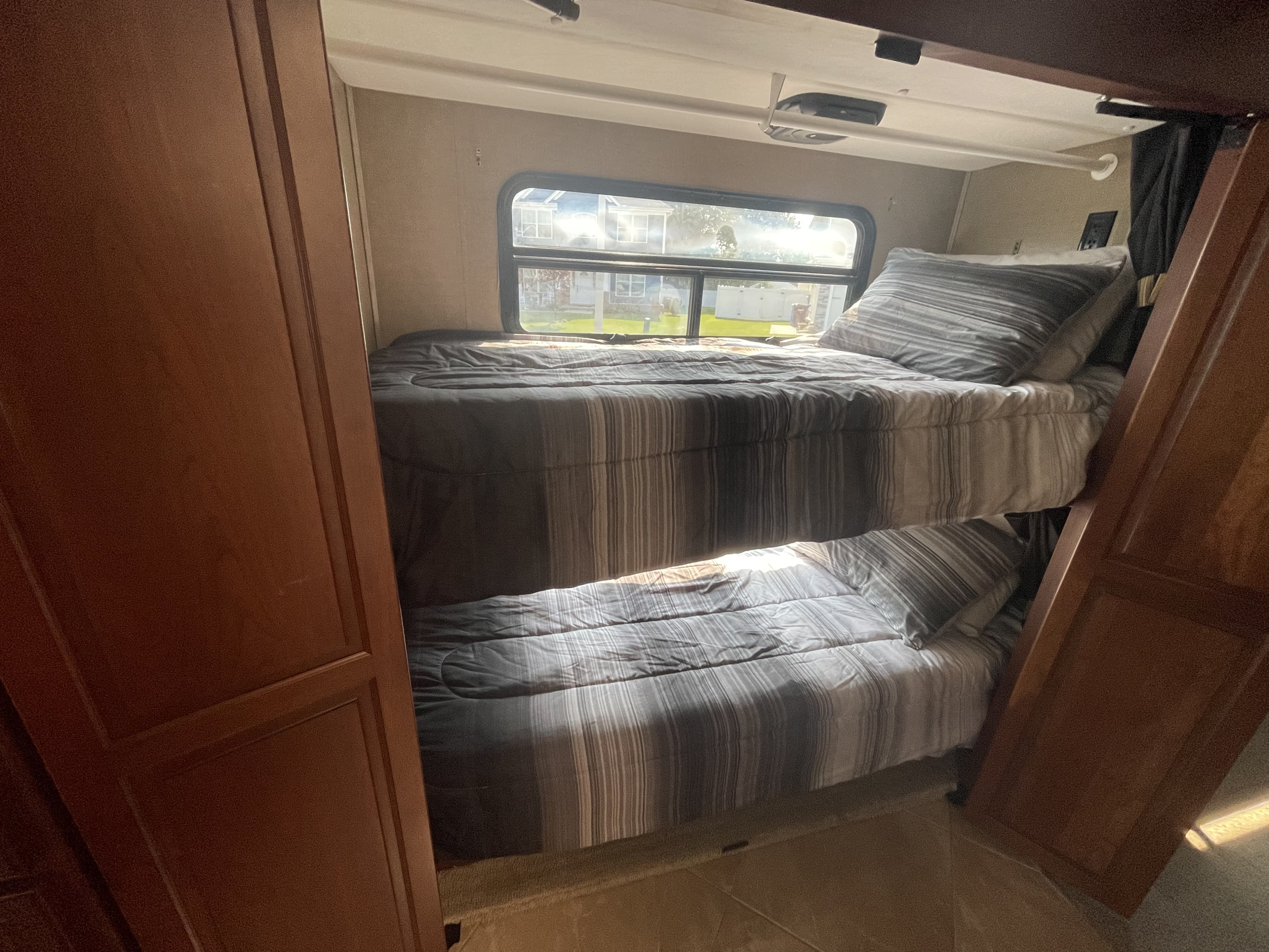 Experience comfortable rv rental adventures! This image shows cozy bunk beds with striped bedding inside an RV, sunlight streaming in.. Forest River Berkshire 2016