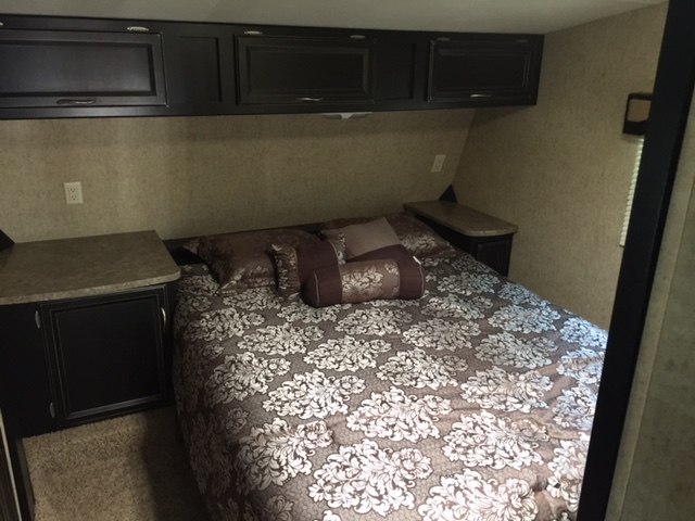 Cozy RV rental bedroom featuring dark cabinets, small nightstands, and patterned bedding.. Heartland Torque 2015