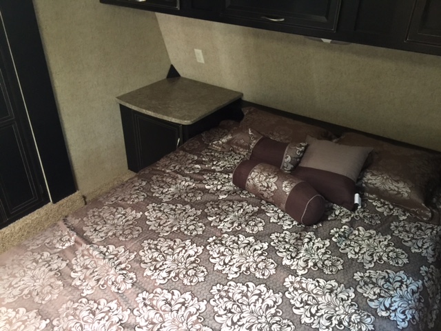 Spacious RV rental bedroom showcasing a comfortable bed with elegant bedding, storage cabinets, and a bedside table.. Heartland Torque 2015