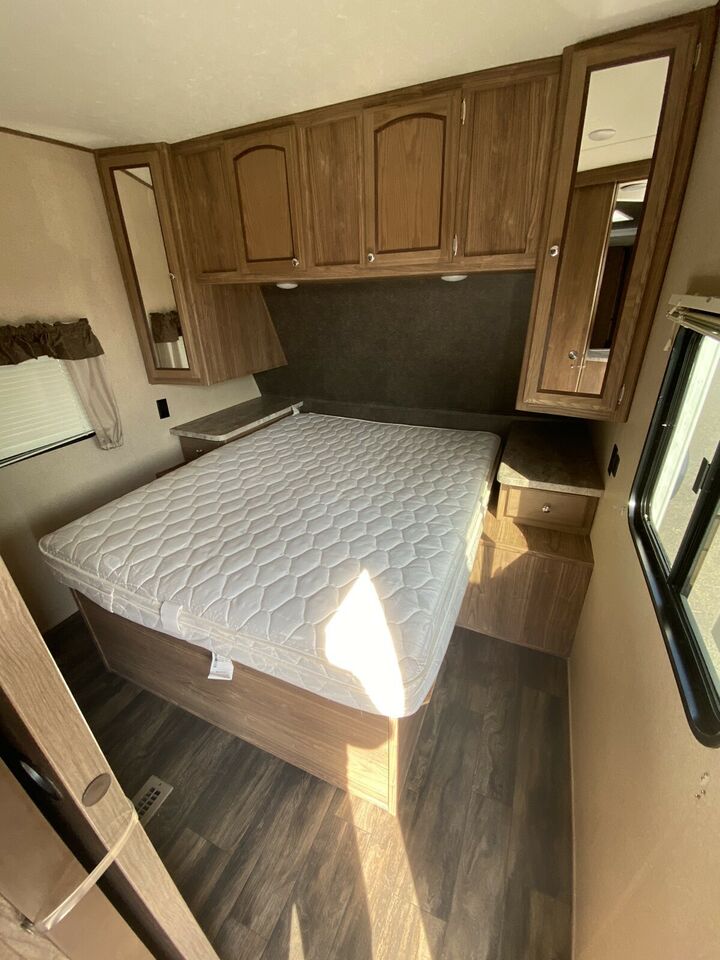 RV rental bedroom featuring a bed, ample overhead wood cabinets, and mirrored cabinet doors.. Forest River Shasta Revere 2018