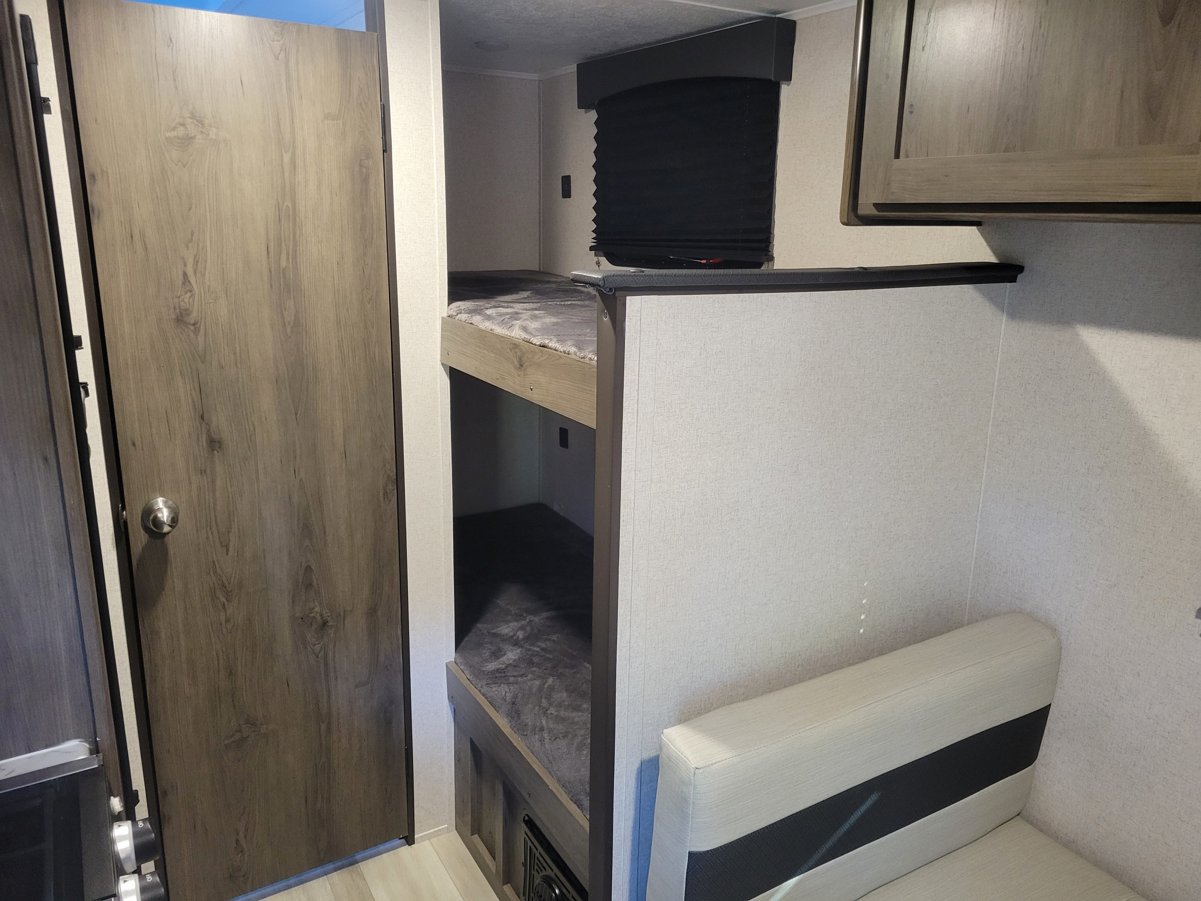 Compact RV rental interior showing bunk beds with gray bedding, a light sofa, and a wooden door. Ideal for family travel.. Coachmen Clipper 2021