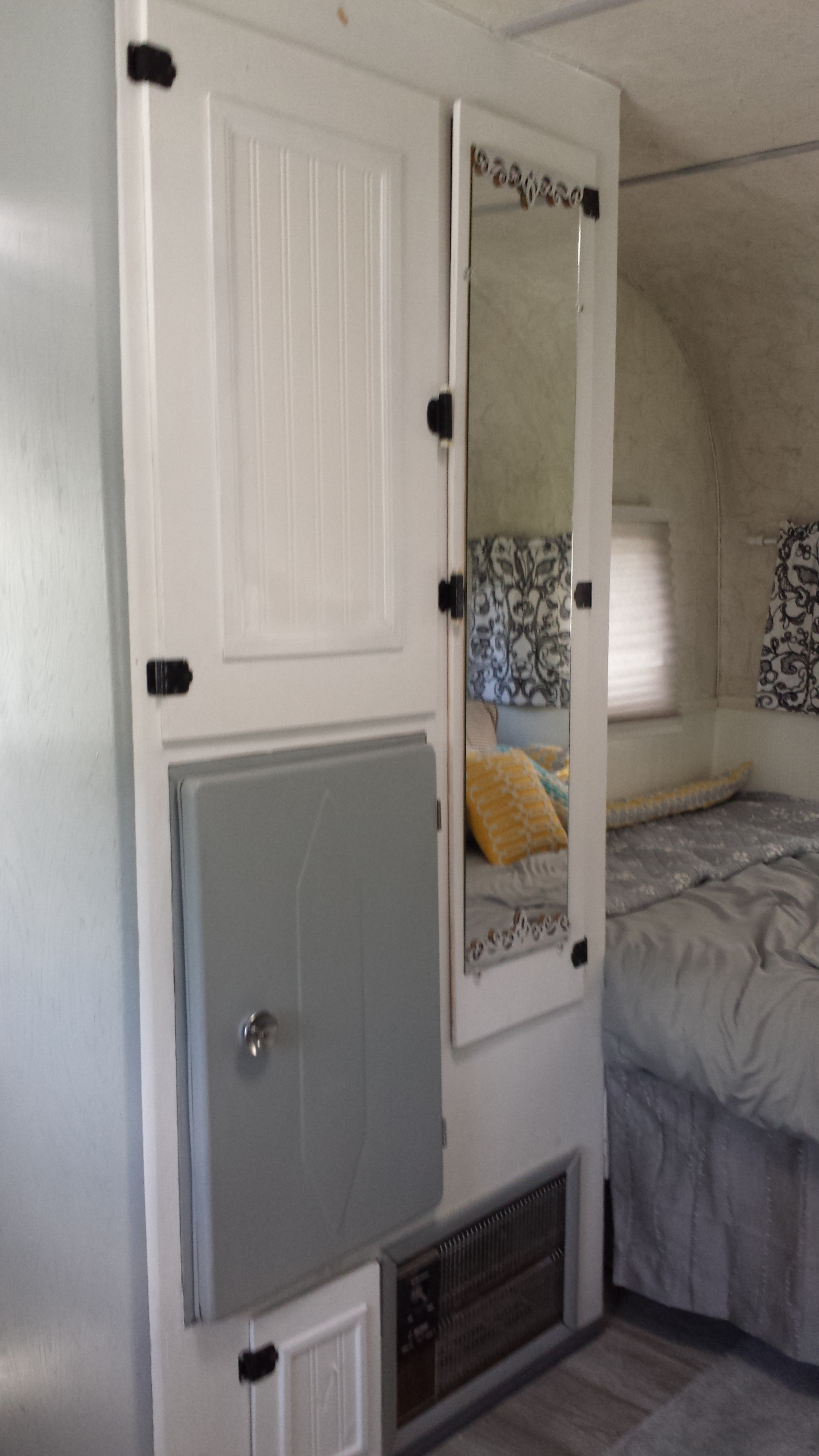 Inside a cozy RV rental: white storage cabinet, integrated mirror showing the bed, and a lower utility panel for convenience.. Vintage Trailers Aloha 1959