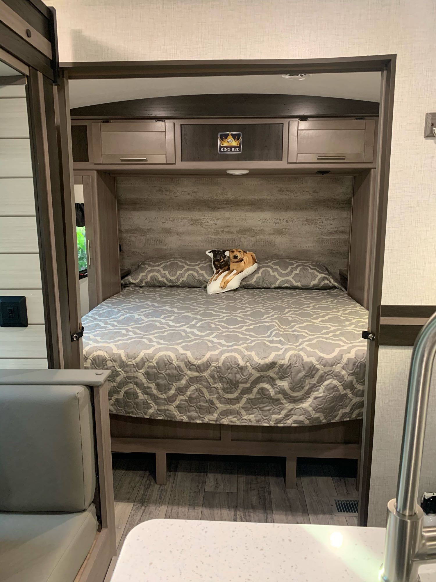 Inside an RV rental: a comfortable king bed with a patterned quilt, a fun dog pillow, and wood-toned cabinets.. Other Other 2021