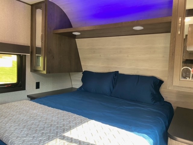 Relax in this RV rental bedroom. Features a comfortable bed with blue bedding, ambient purple light, and storage.. Jayco Jay Flight SLX 2021
