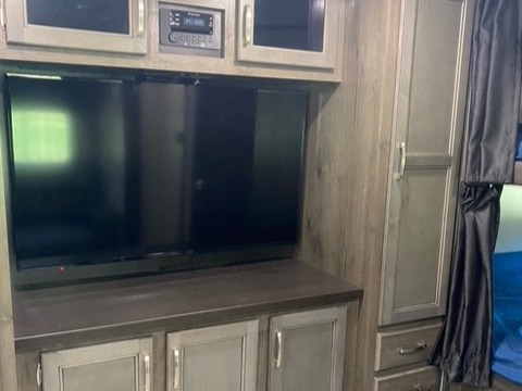 RV rental: Entertainment center with TV, overhead/lower cabinets, wardrobe, & adjacent sleeping area with curtains.. Jayco Jay Flight SLX 2021