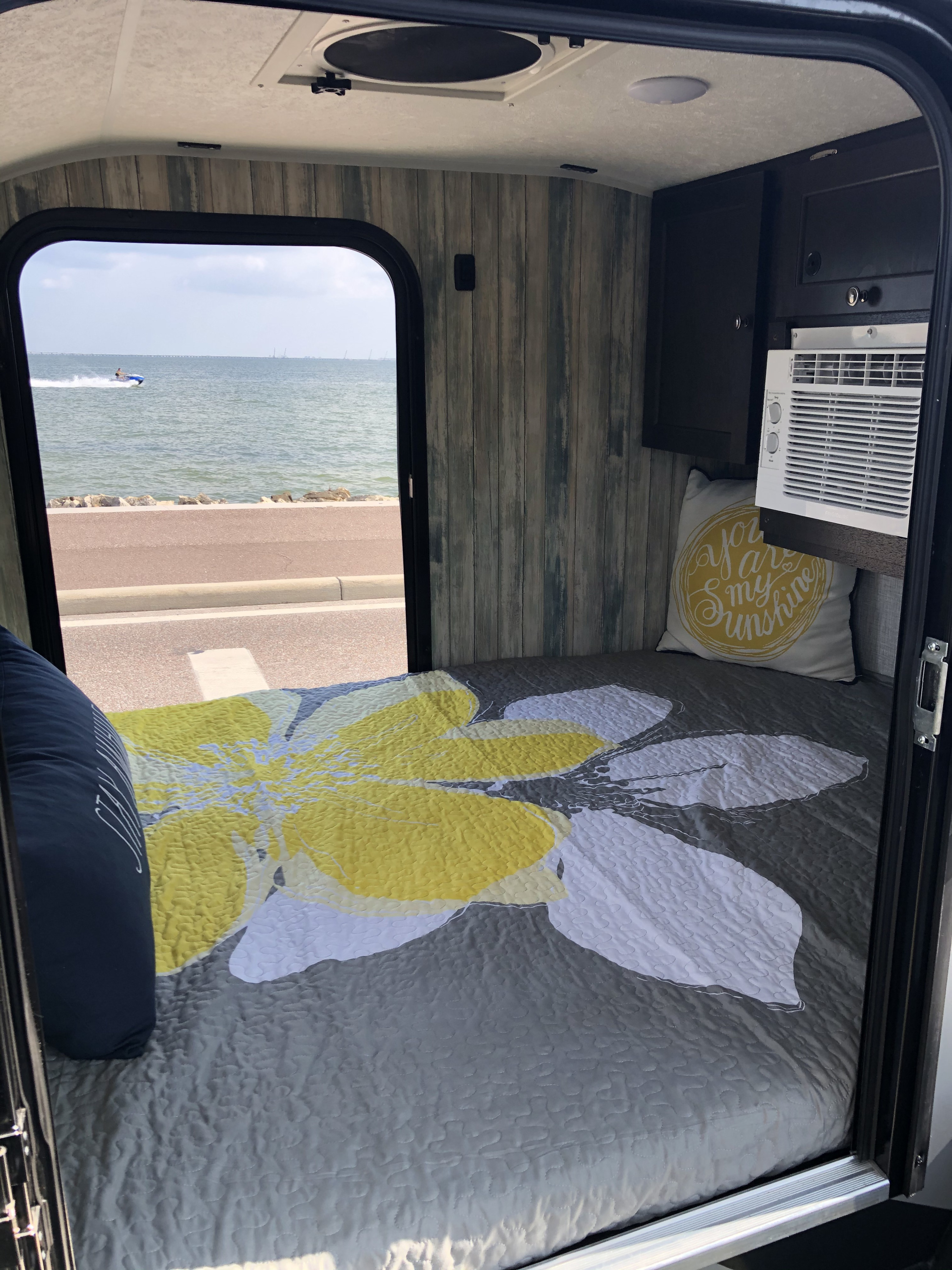 Cozy RV rental interior with a comfortable bed, AC unit, and a scenic waterfront view with a jet ski.. Braxton Creek Free Solo 2021
