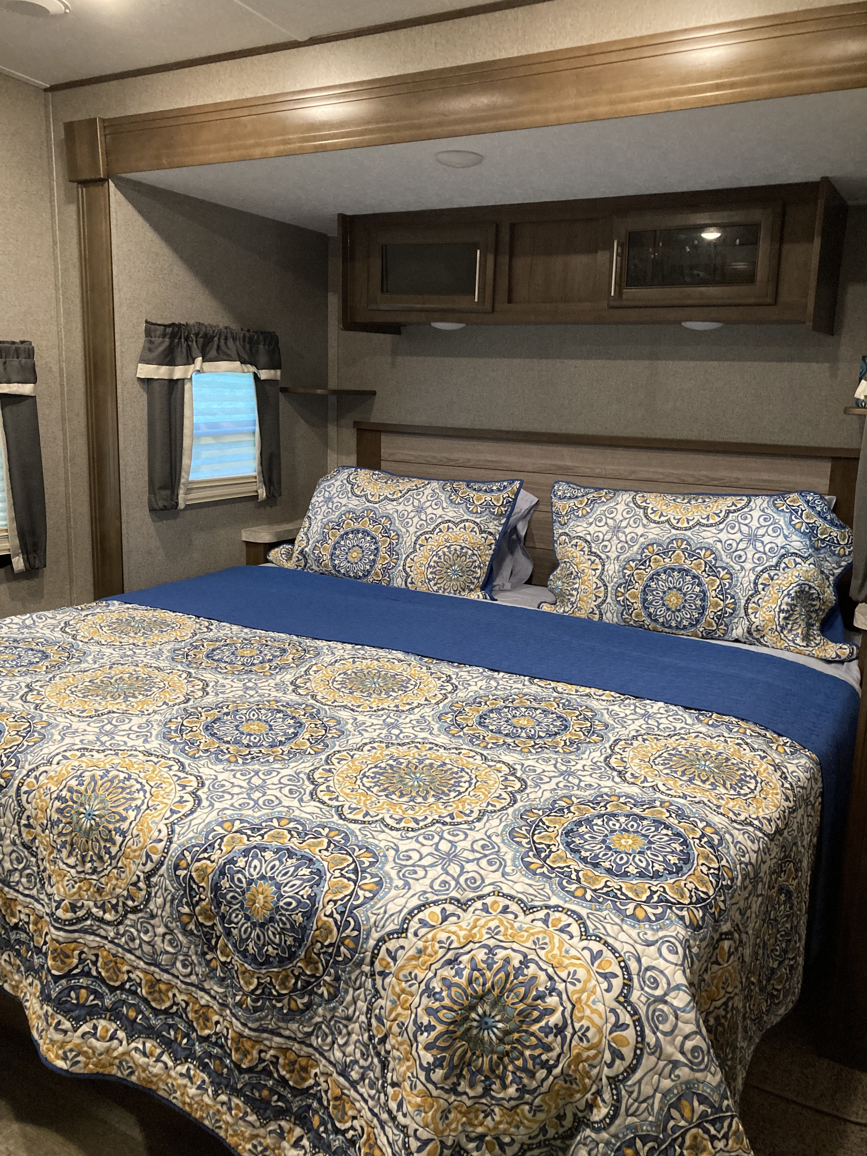 RV rental bedroom with a bed featuring a blue, gold & white patterned comforter, matching pillows, wood headboard & cabinets.. Forest River Rockwood Signature 2021