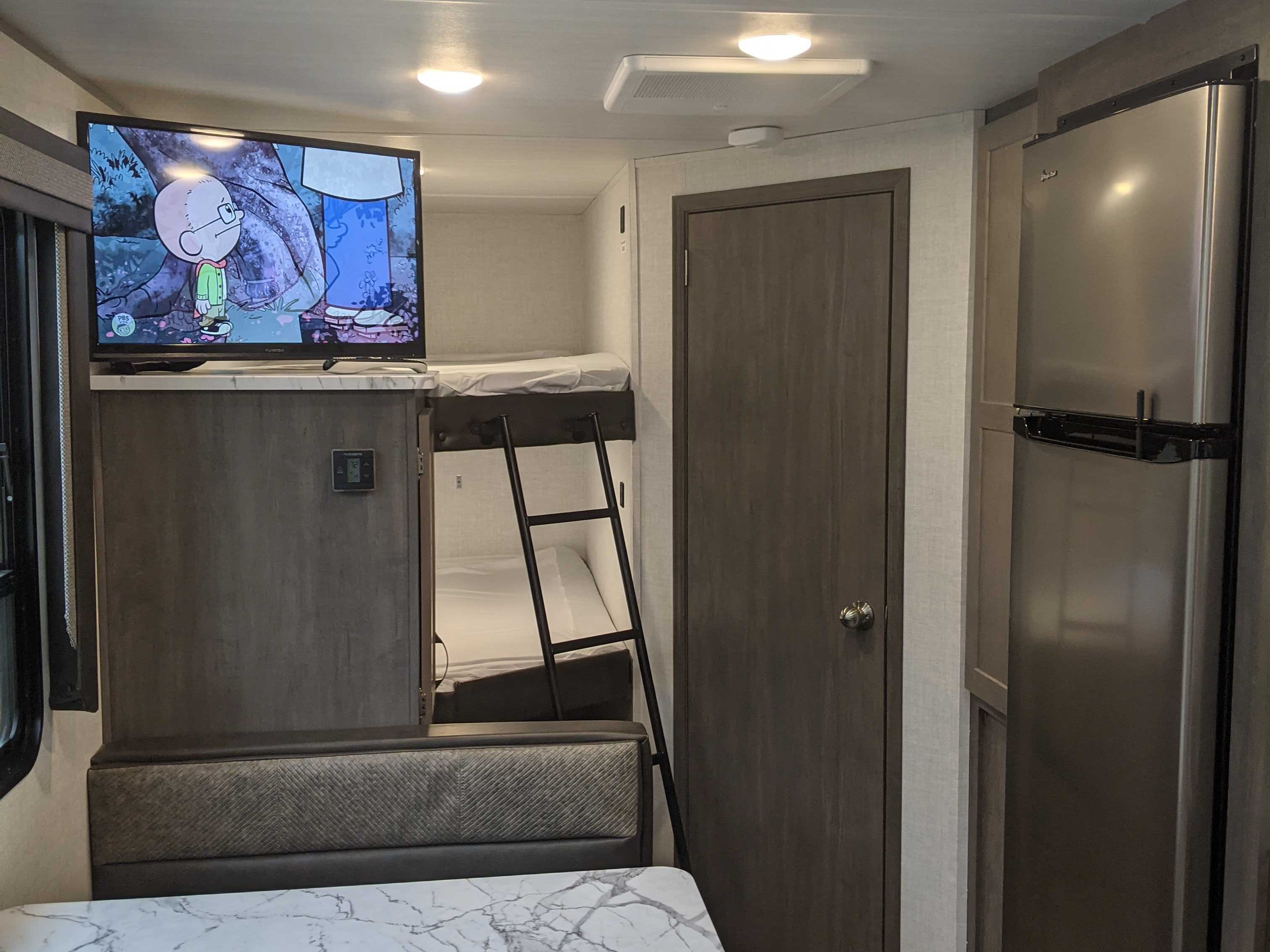 Compact RV rental interior with TV, bunk beds, a ladder, refrigerator, and dinette seating. Ideal for travel comfort.. East to West Alta 2021