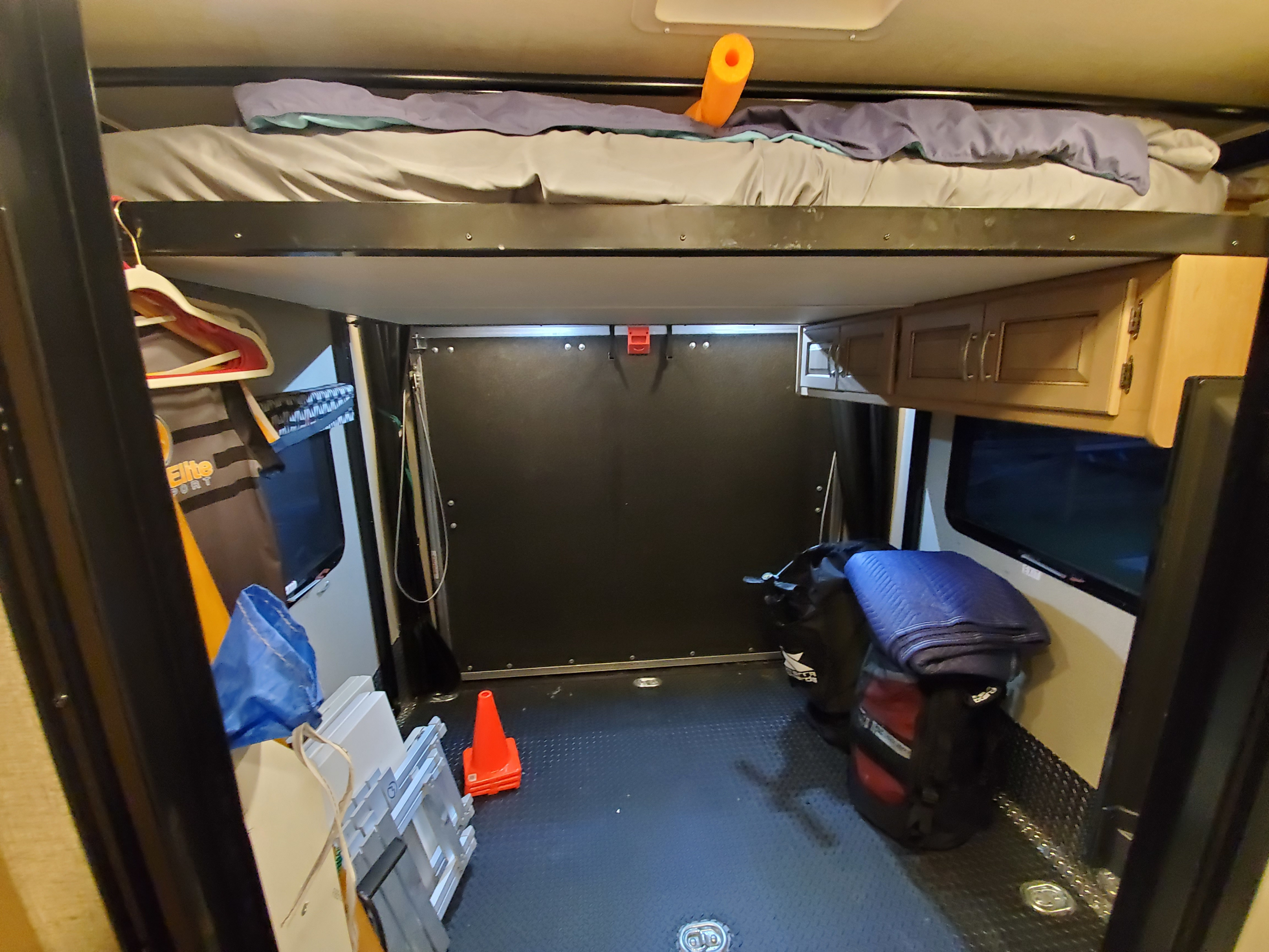 Inside an rv rental, featuring a raised bunk bed, diamond plate cargo floor, and cabinets, ideal for adventure gear.. Thor Motor Coach Outlaw 2021