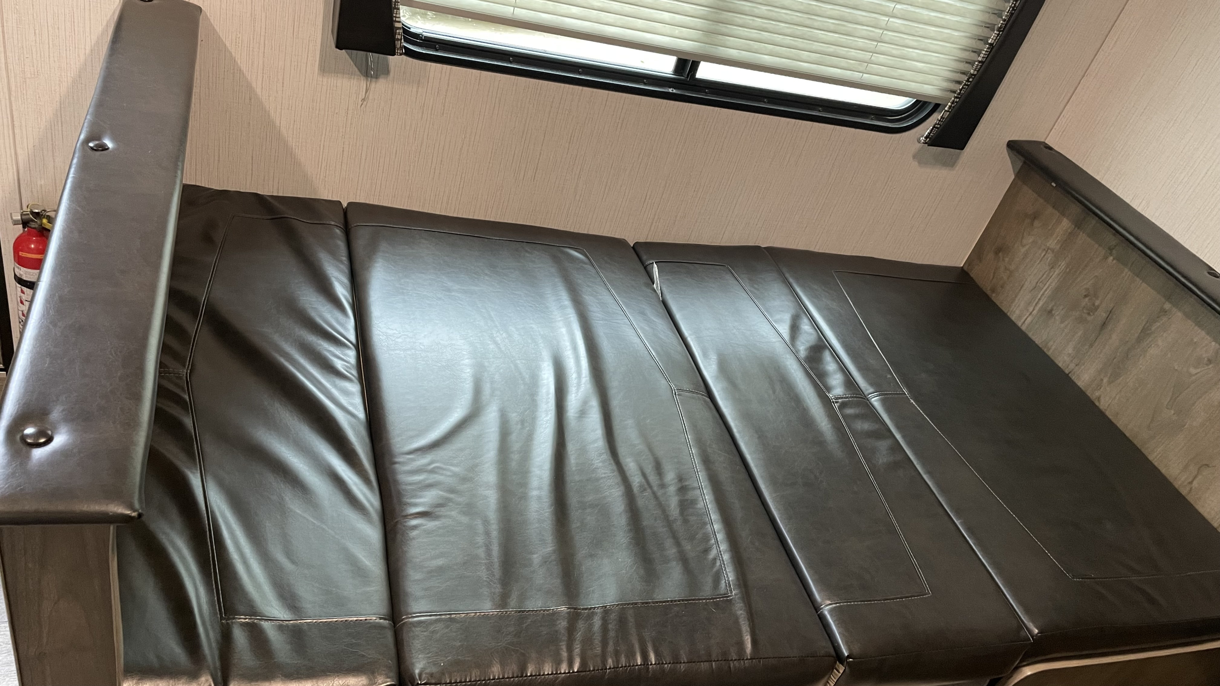 RV rental interior: a dark brown convertible dinette seat/bed with window, blinds, and a visible fire extinguisher.. Heartland RVs Pioneer 2021