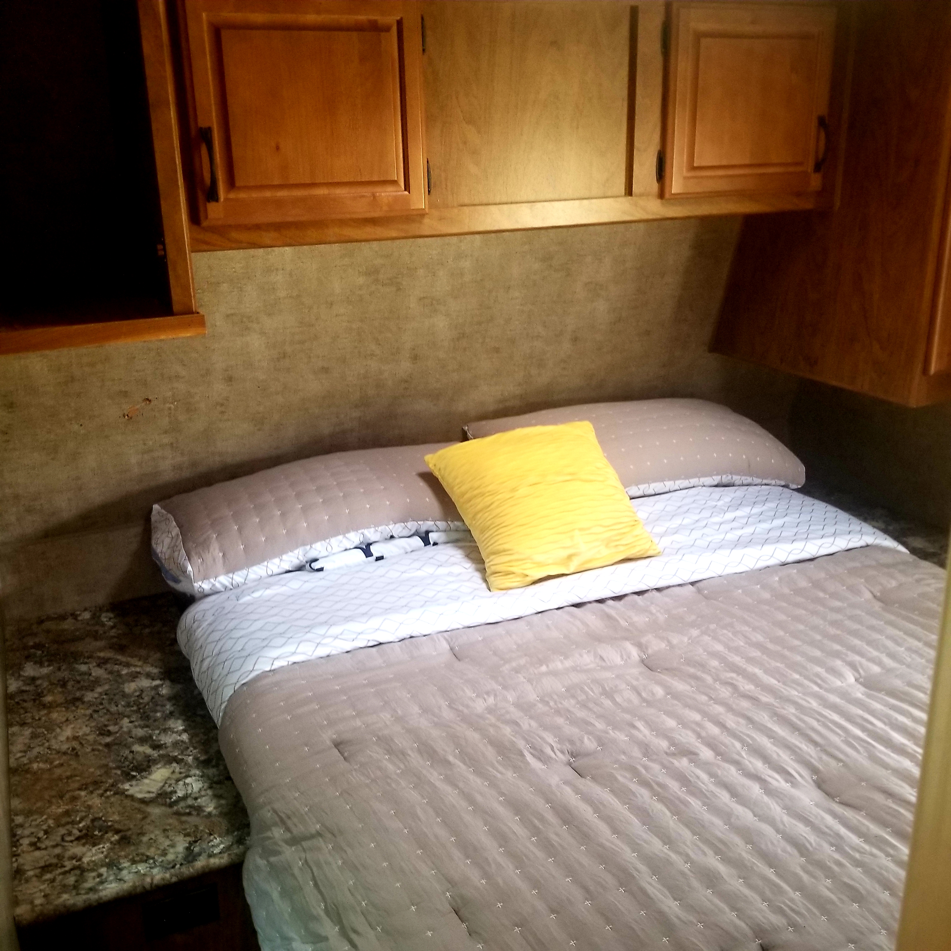 This RV rental shows a cozy bedroom with a comfortable bed, bright yellow pillow, wood cabinets, and counter.. Outdoors Rv Manufacturing Creek Side 2016