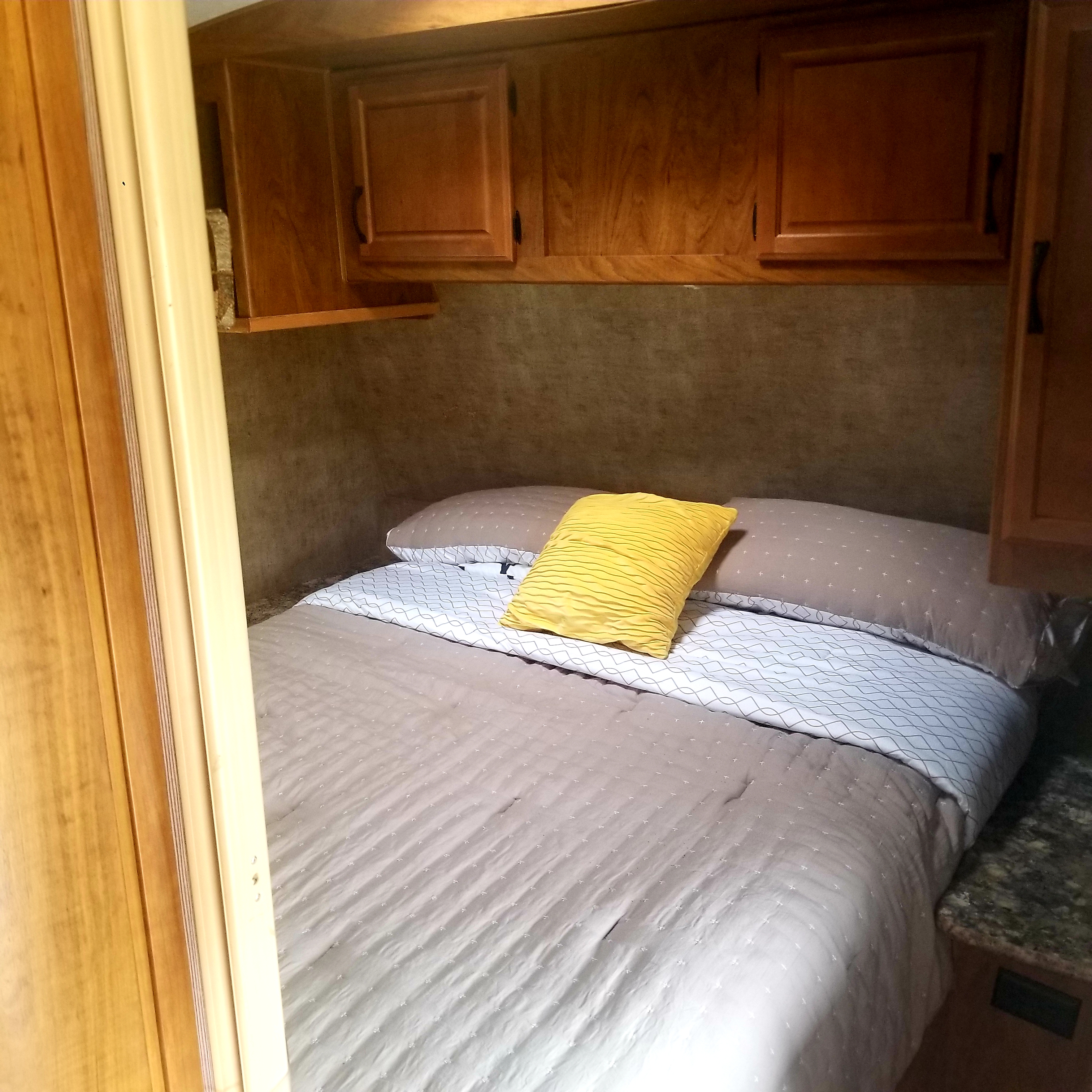 Comfortable RV rental bedroom featuring a neatly made bed with a yellow pillow and overhead cabinets.. Outdoors Rv Manufacturing Creek Side 2016
