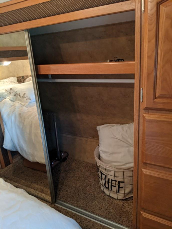 Inside an RV rental bedroom: a mirrored closet reveals a compact storage area with a shelf, hanging bar, vacuum, and 'STUFF' basket.. Keystone Cougar 2009