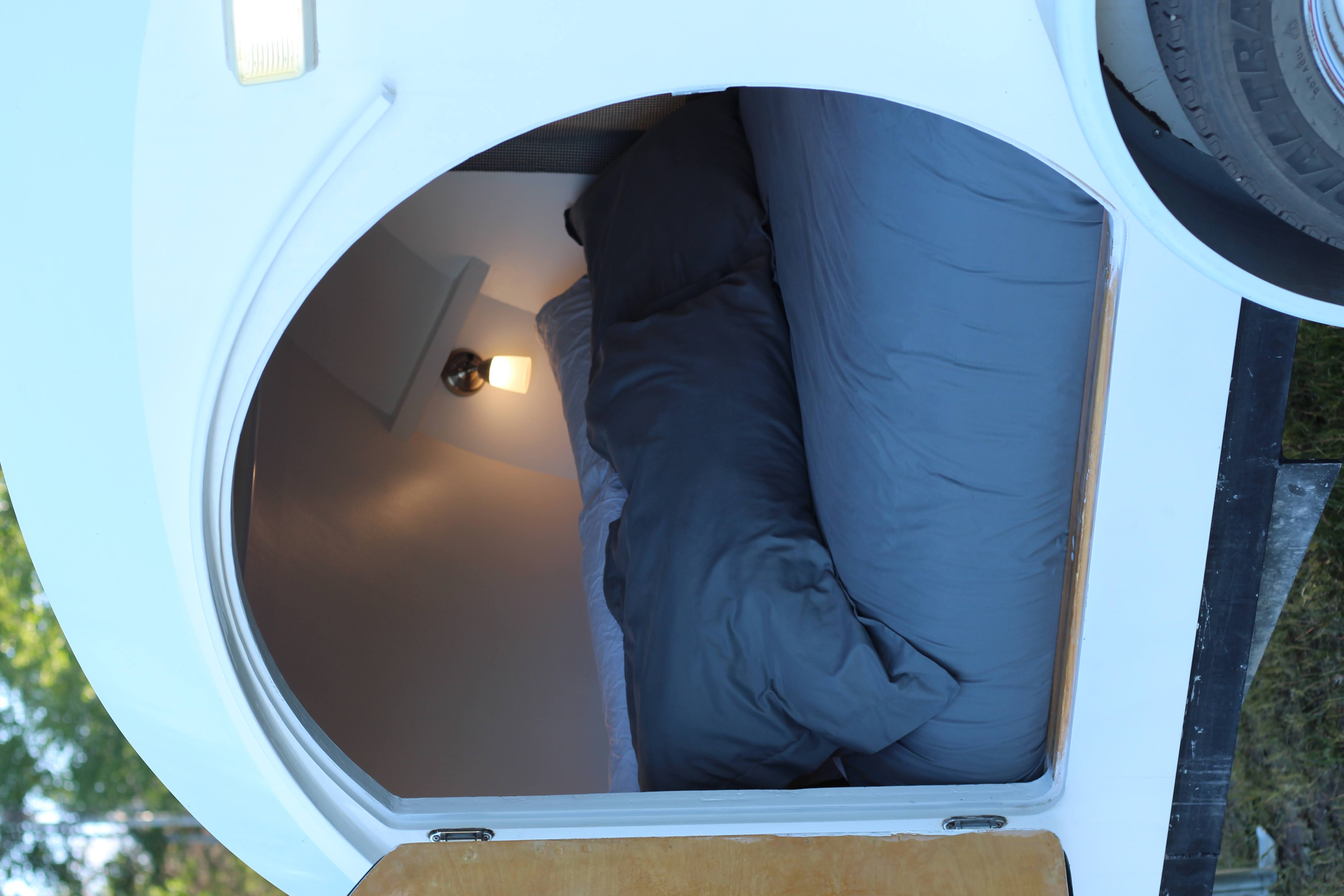 Cozy interior of a compact RV rental, showing a comfortable bed and light fixture. Ideal for adventurous travel.. Custom Teardrop 2019