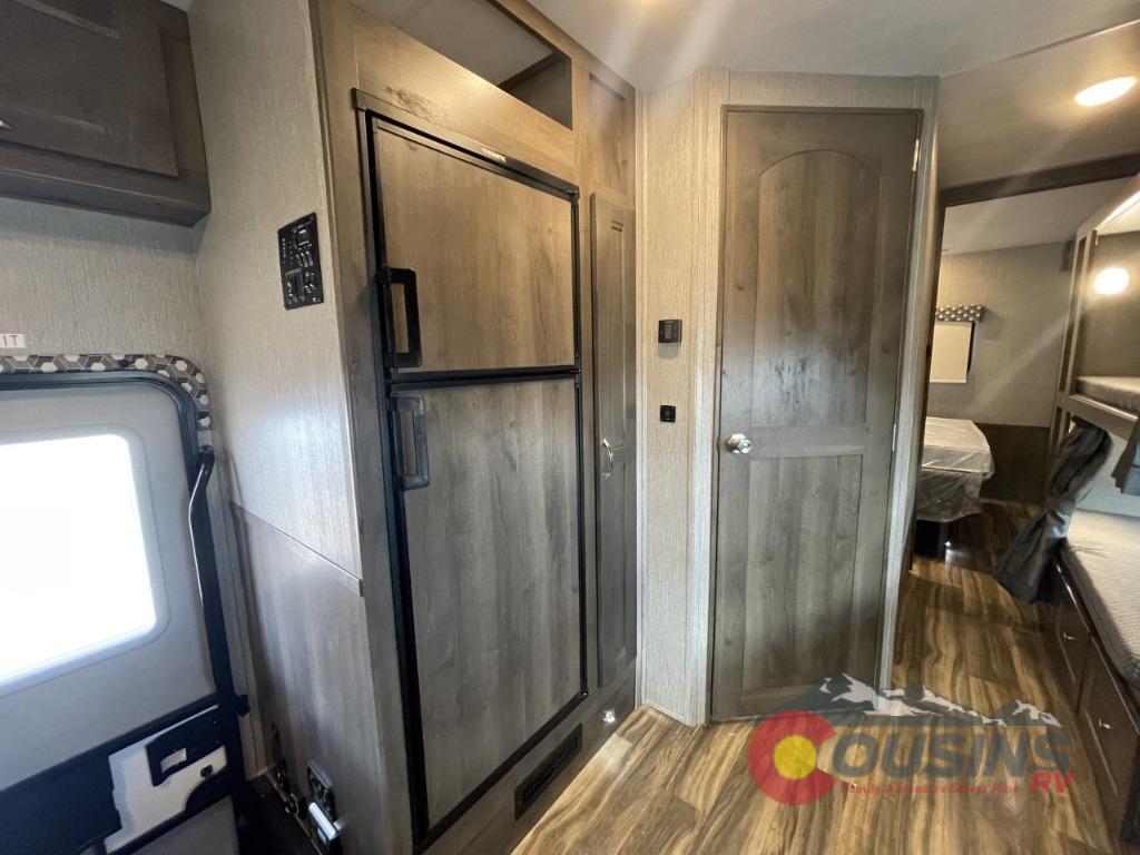 Inside this RV rental: functional kitchen area with fridge, access to bedroom/bunks, and entry door. Ready for travel!. Nexus Rebel 2022