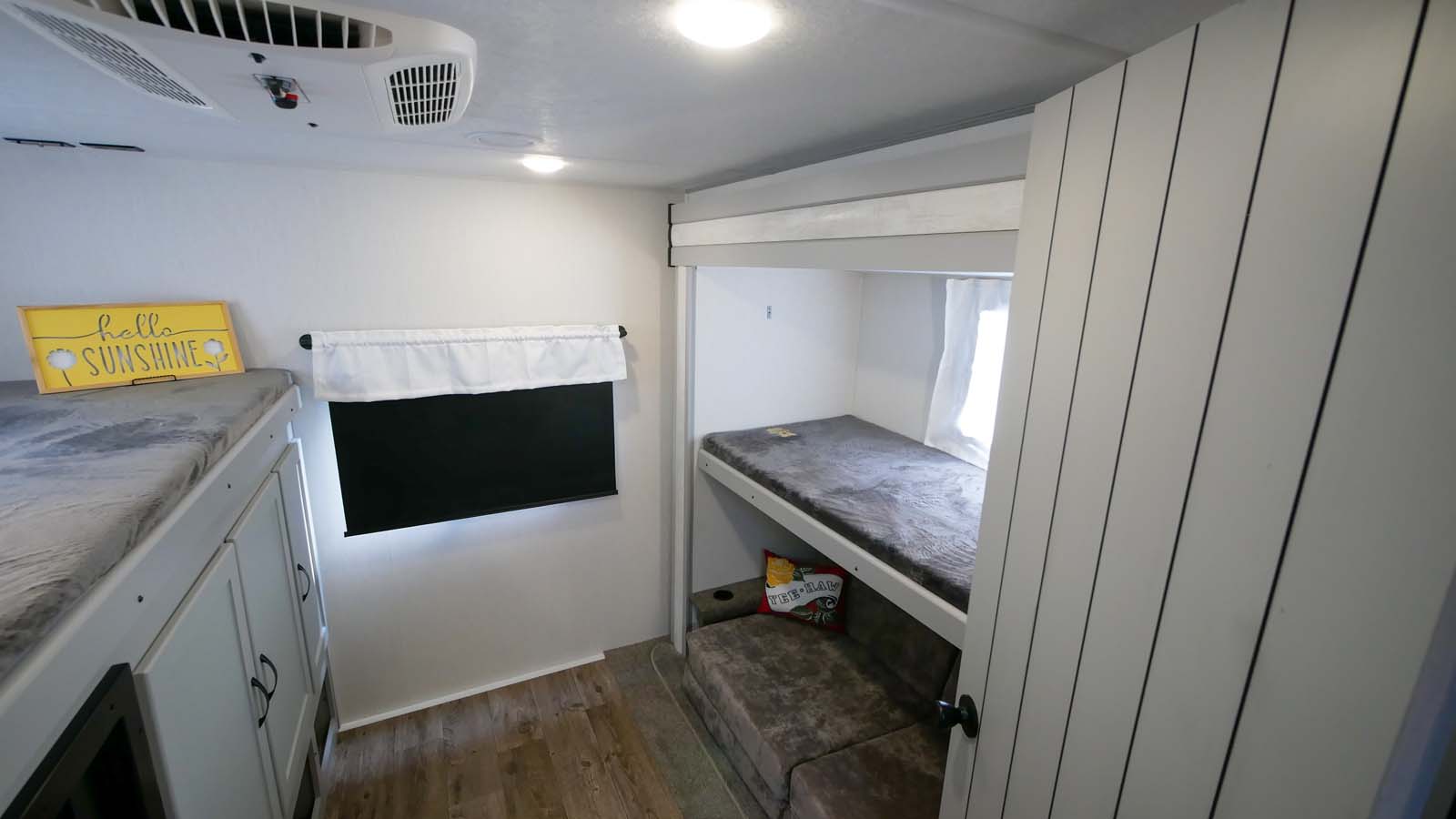 RV rental bunkhouse: two bunks, one with "hello sunshine" sign, another above a sofa bed. AC unit overhead.. Forest River Vibe 2021