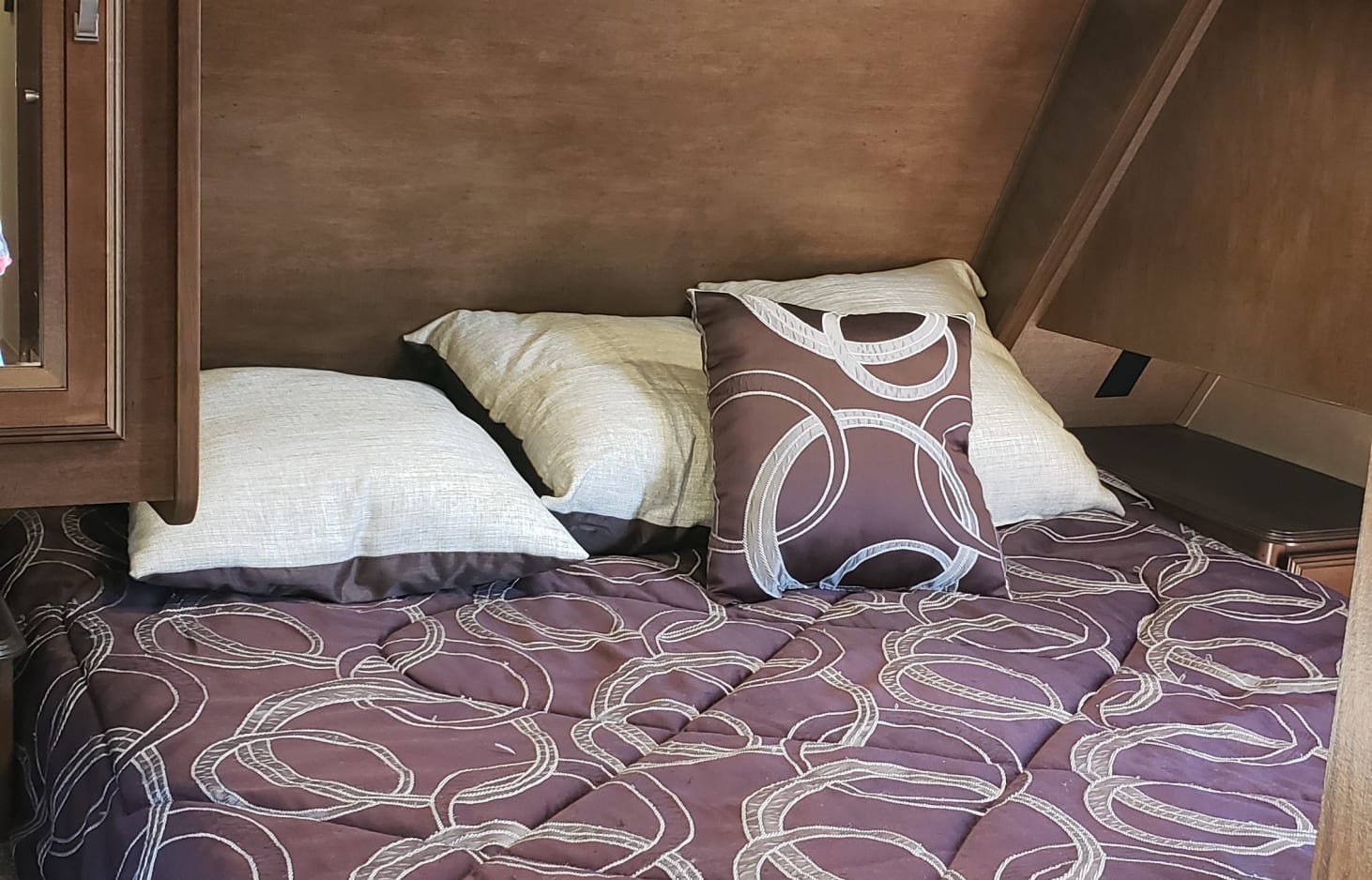 Inside an RV rental: a cozy bedroom with a maroon patterned bed, assorted pillows, and wooden accents for comfortable travel.. Forest River Wildwood Heritage Glen Lite 2016