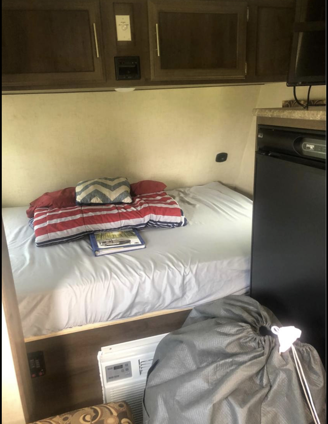 Cozy RV rental interior: bed with red comforter, overhead storage, mini-fridge, and AC unit. Ready for adventure.. K-Z Manufacturing Sportsman Classic 2018