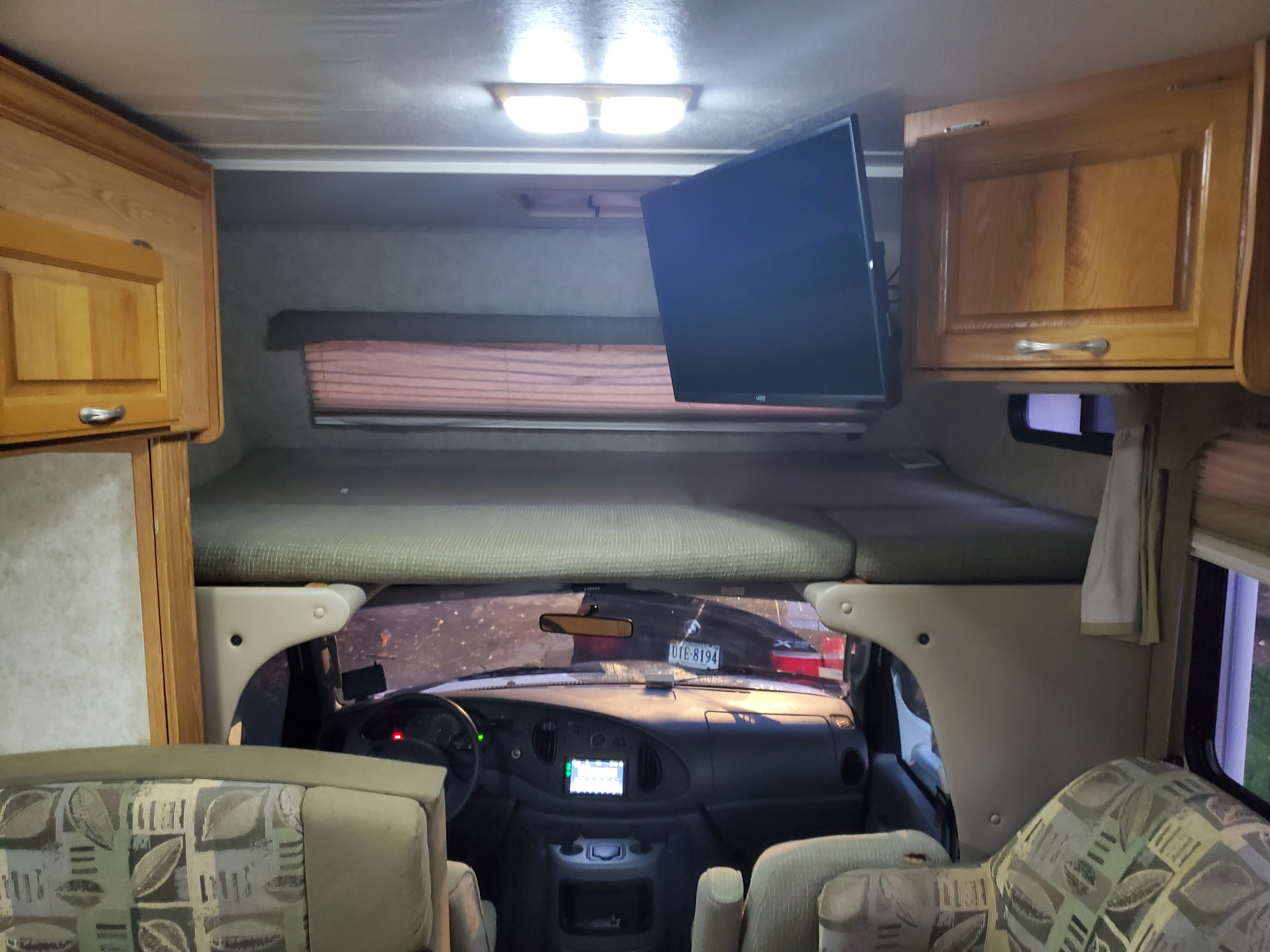 Inside this **rv rental**, featuring an over-cab bunk bed, mounted TV, and the driver's cabin ahead.. Thor Motor Coach Four Winds 2004