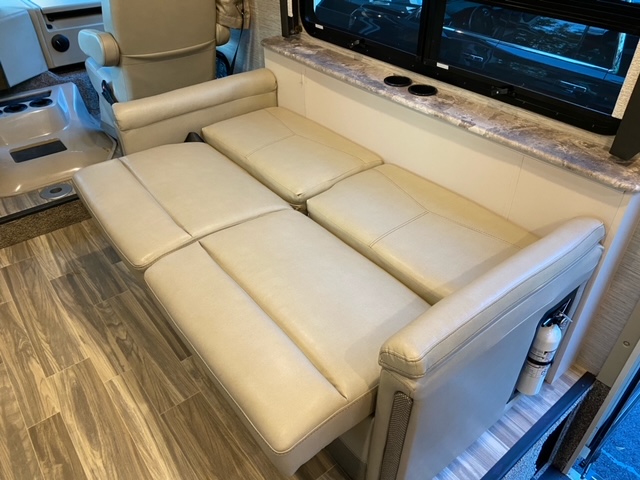 RV rental interior: Beige convertible sofa extends, with window, countertop, and fire extinguisher. Ideal for comfortable travel.. Thor Motor Coach A.C.E 2021